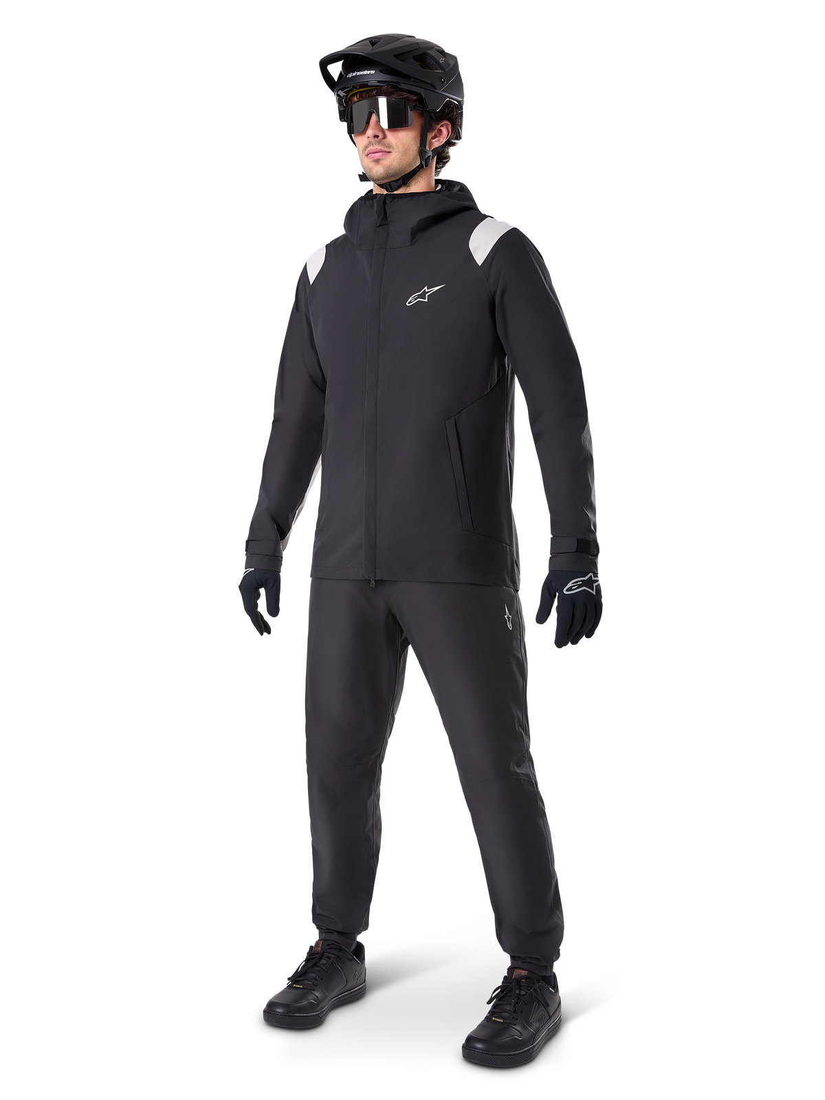 Alpinestars A-Dura Rain Jacket, Black Mountain Bike Rain Jacket, featuring white shoulder accents, worn by a rider with matching black MTB helmet, sunglasses, gloves, and pants, technical all-weather cycling outfit