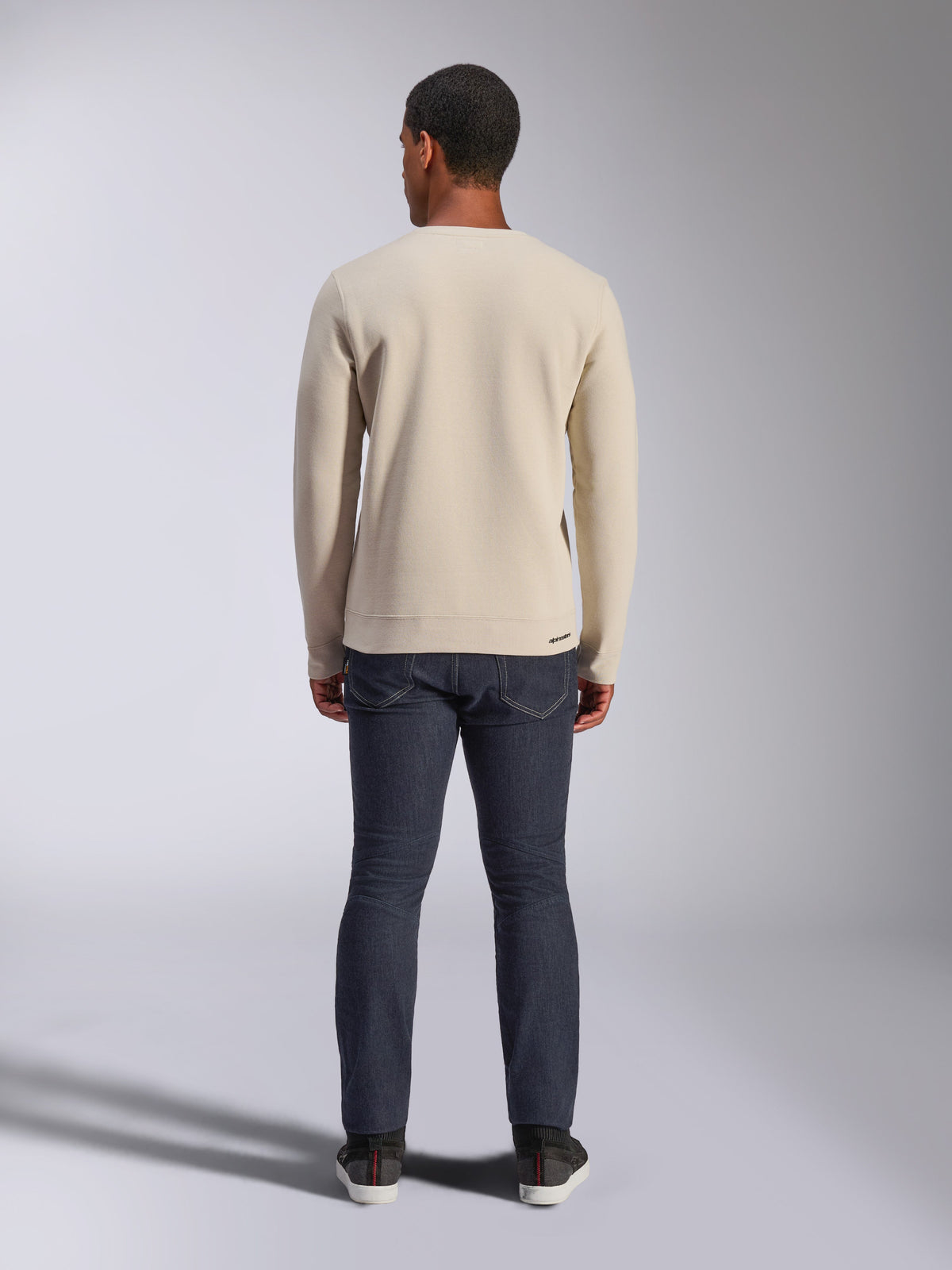Alpinestars Positive Crew Sweatshirt, Off White, back view of a man wearing a beige crewneck pullover with ribbed hem and cuffs, paired with dark jeans, casual motorsport-inspired streetwear.