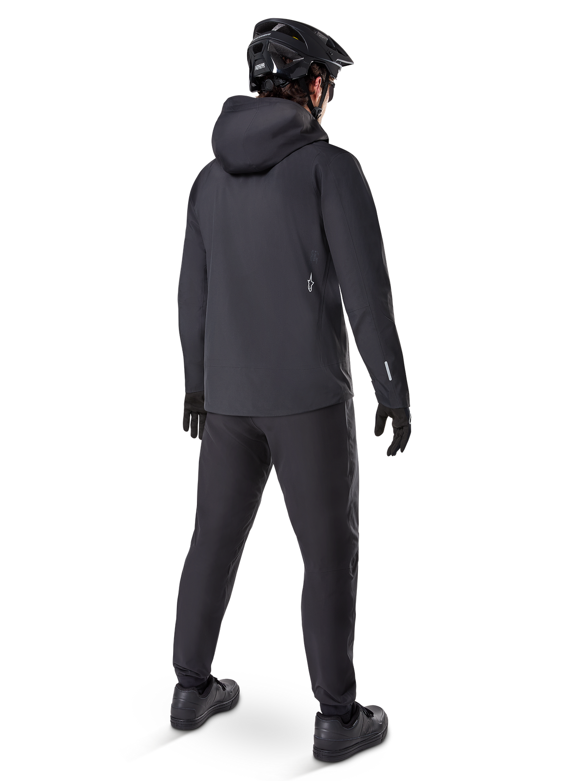 Alpinestars A-Dura Elite Waterproof Jacket, Black, rear view showing over-the-helmet hood and longer drop tail hem, paired with matching black MTB pants, gloves, and helmet for complete all-weather trail protection.
