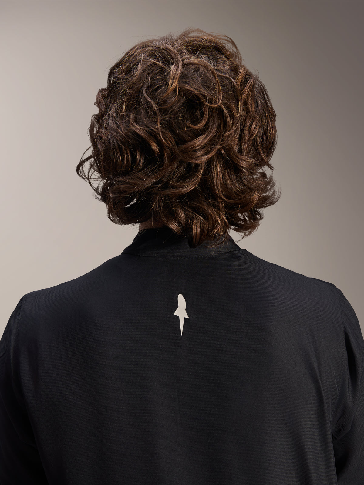 Alpinestars A-Aria Windbreaker Jacket, Black, close-up back view of upper shoulders and collar, featuring a small white logo on the center back, worn by model with wavy brown hair, minimalist performance cycling gear