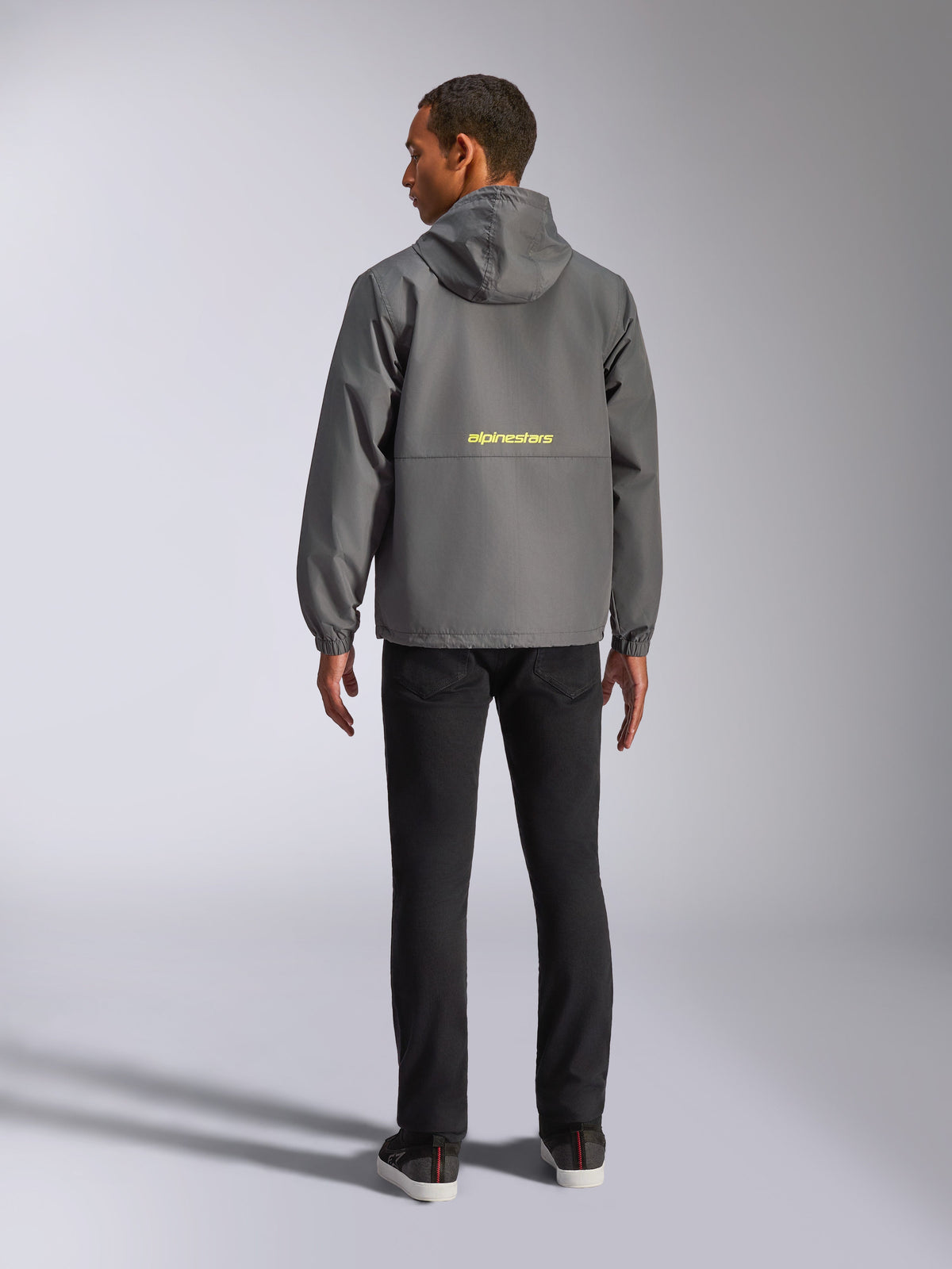 Alpinestars Speeder Chromium Windbreak Jacket, Charcoal and Hi Vis Yellow, back view showing yellow Alpinestars logo across the center, lightweight windbreaker with hood and elastic cuffs, casual motorsport-inspired streetwear