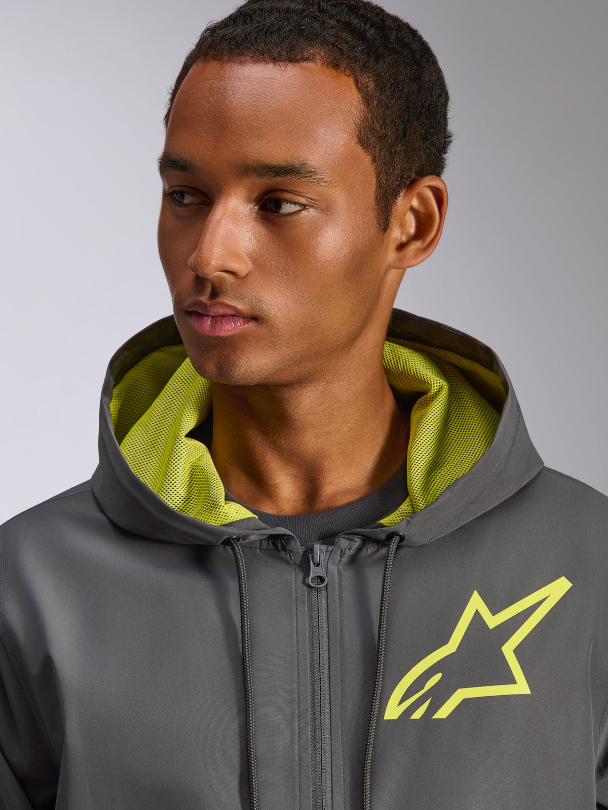 Alpinestars Speeder Chromium Windbreak Jacket, Charcoal Grey with Hi-Vis Yellow accents, featuring a yellow star logo on the chest and matching mesh hood lining, lightweight casual windbreaker