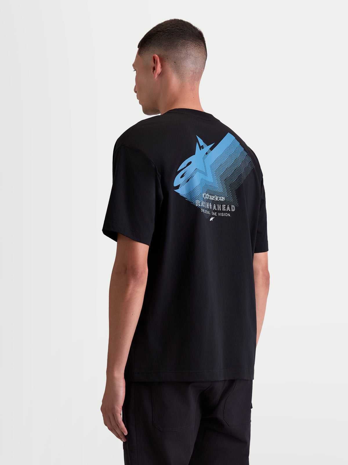 Alpinestars Ghost Oversized CSF Tee, Men’s Short Sleeve Sportswear T-shirt, Black with Blue graphic. Back view on model showing a large Astars fade logo with 'Racing Ahead' and 'One Goal. One Vision.' text. Relaxed oversized fit in a soft cotton-poly blend for casual off-bike wear.