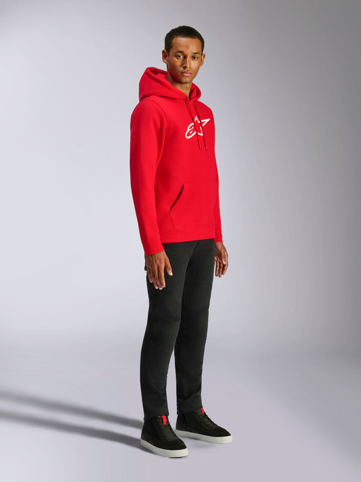 Alpinestars Ageless V3 Hoodie, Red with White Embroidered Logo, casual sportswear hoodie worn by a man with black pants and black sneakers, featuring a drawstring hood and ribbed cuffs