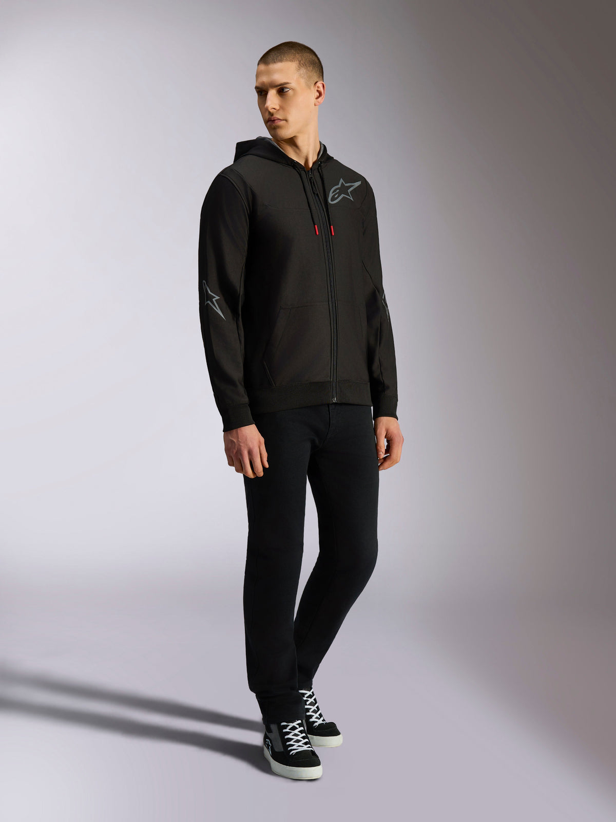 Alpinestars Sessions V3 Hoodie, zip front poly fleece, Black and Grey, grey chest and sleeve logos, drawstring hood with red-tipped drawcords, full-body view of model in casual motorsport streetwear