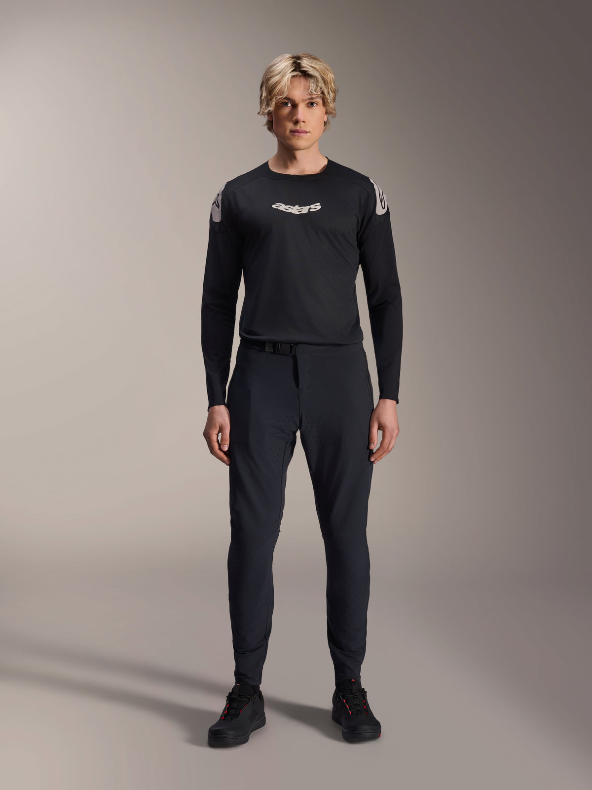 Alpinestars A-Aria Elite Pants, Black Titanium MTB Pants, worn by a male model with a matching black long-sleeve jersey and sneakers, slim-fit performance design with magnetic buckle closure, technical mountain bike apparel