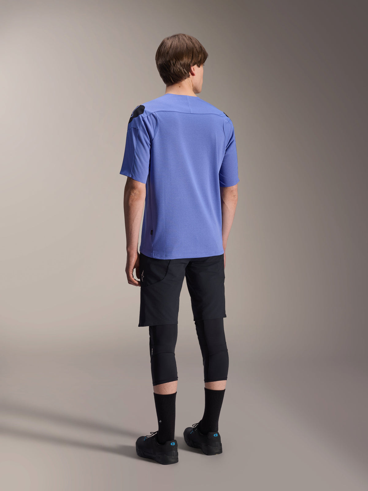 Alpinestars A-Aria Polartec Elite Short Sleeve Jersey in Baja Blue, back view on a male model, paired with black MTB shorts and knee protection, featuring a performance fit and dropped rear hem for trail riding.