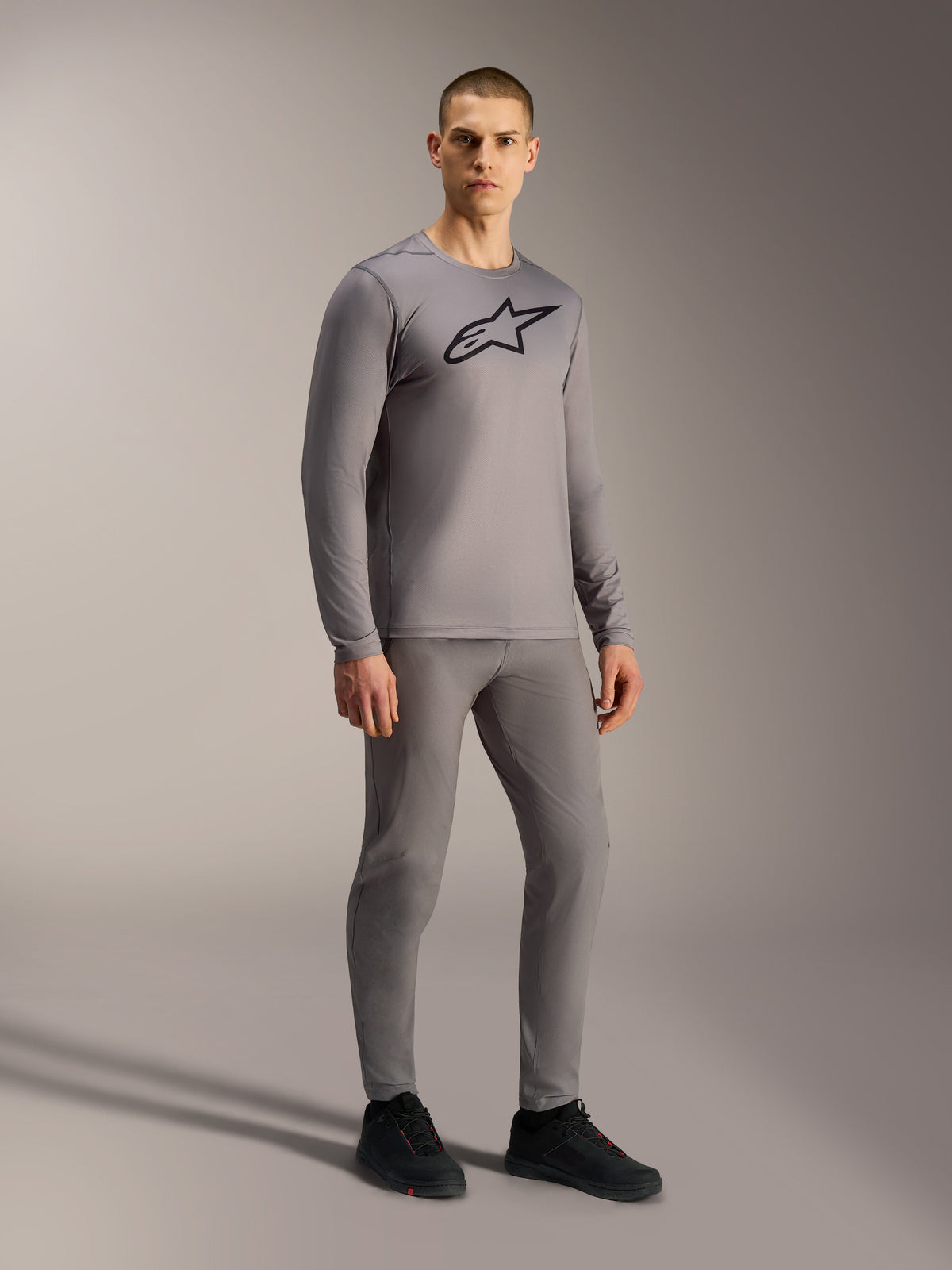 Gray A-Dura Ride Long Sleeve Jersey featuring a black chest logo, styled on a model for a complete mountain biking look.
