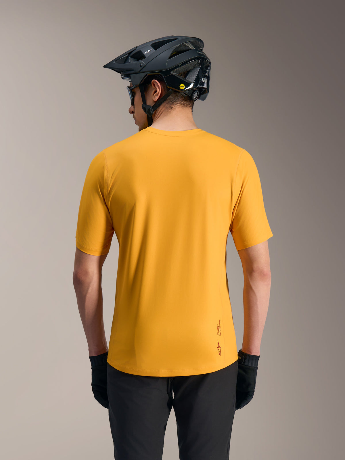 Orange A-Dura Ride Short Sleeve Jersey, lightweight MTB top with drop tail and logo, shown from the rear with a helmet.