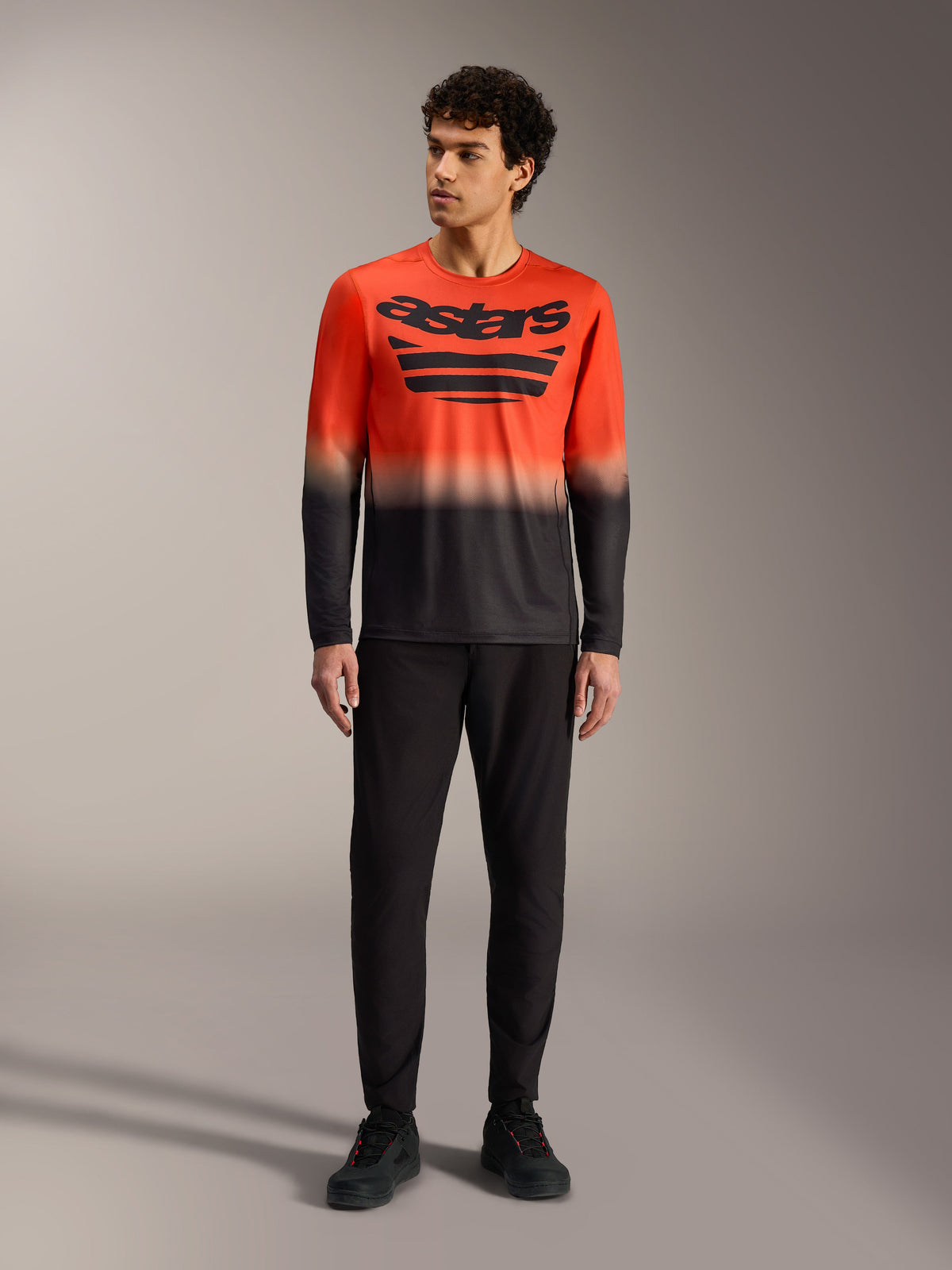 A-Dura ASTARS Long Sleeve Jersey 2.0 in orange and black gradient with large chest logo, paired with black MTB pants.