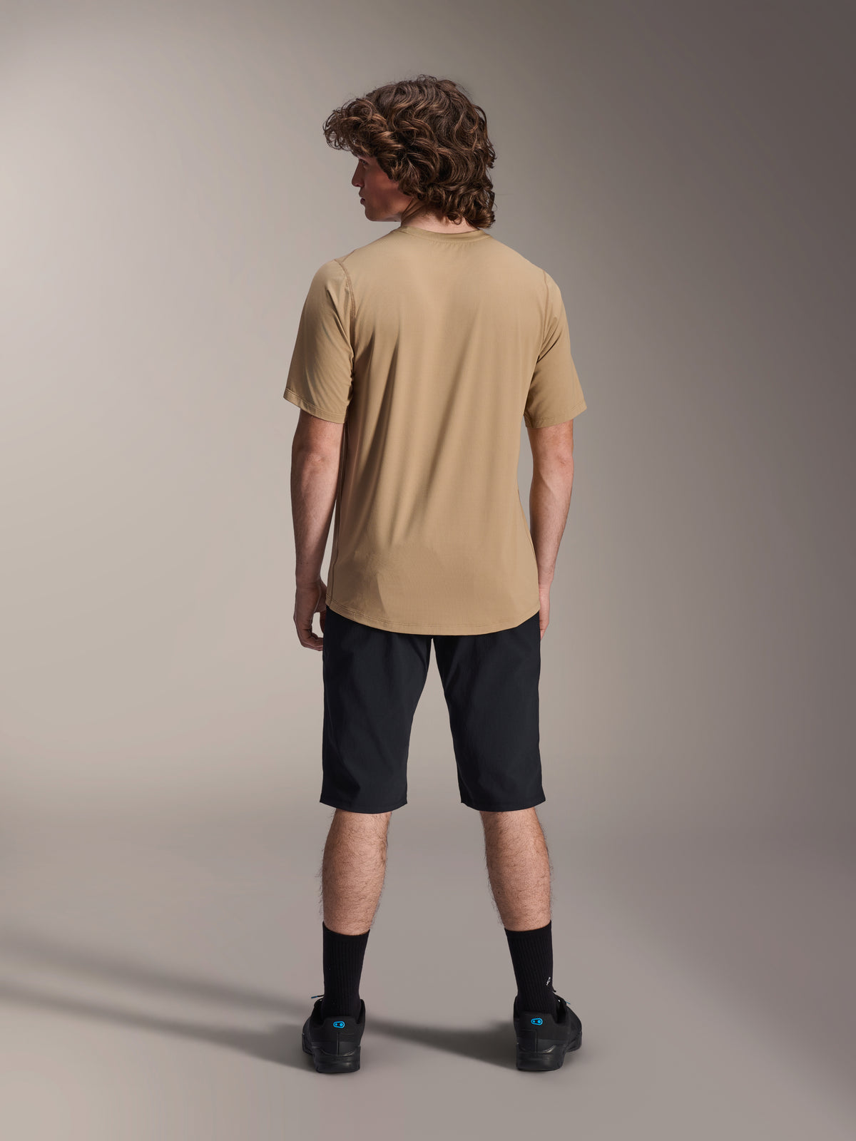 Male model from the back wearing Alpinestars A-Dura Shorts in Black and a tan A-Dura Short Sleeve Jersey, paired with black socks and mountain bike shoes, functional MTB trail outfit