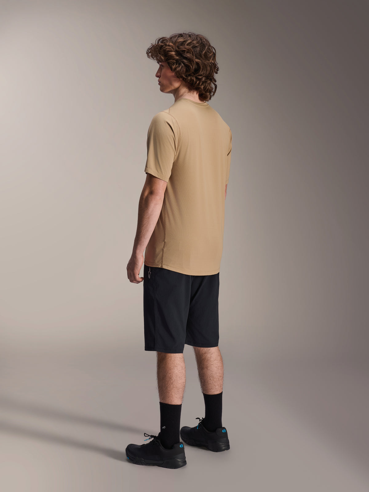 Alpinestars A-Dura Liner Shorts in Black and A-Dura SS Jersey in Tan, worn by a male model from a side profile view, paired with black socks and cycling shoes, mountain bike lifestyle apparel.