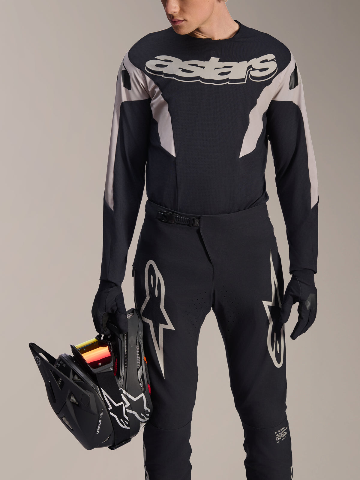 Alpinestars A-Supra Melt MTB Racing Kit, Long Sleeve Jersey and Pants, Black and Grey with white Astars logos, model holding a black full-face helmet and wearing matching gloves, high-performance gear for downhill and enduro mountain biking