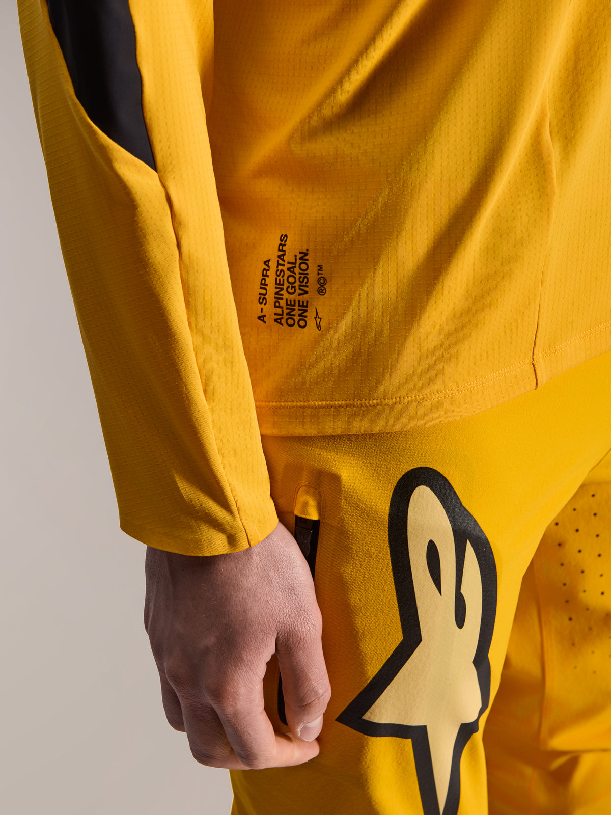 Alpinestars Limited Edition A-Supra Melt Gold Pants and matching LS Jersey, Dark Yellow, close-up view featuring 'One Goal. One Vision.' branding and large stylized logo on the thigh, high-performance MTB gear