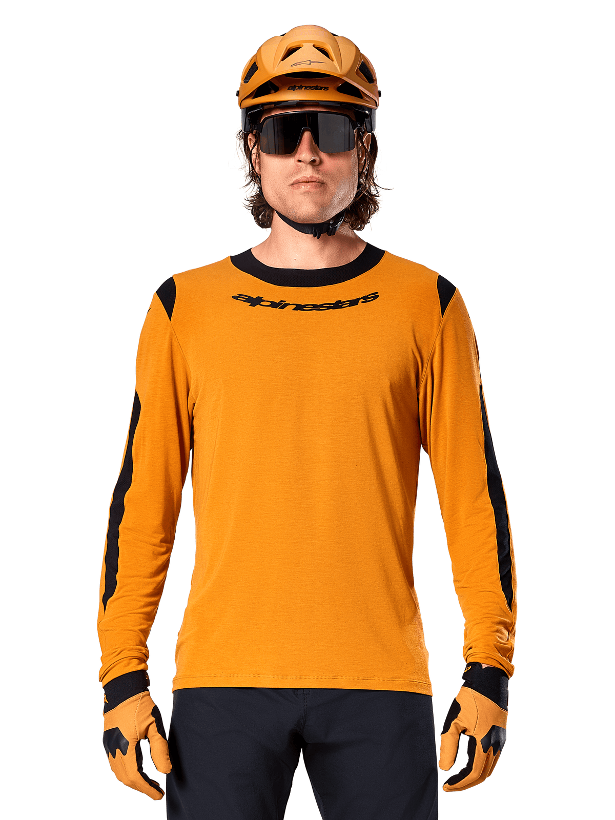 Male model wearing Alpinestars A-Dura Dri Wool Long Sleeve Jersey in Dark Gold, coordinated with a matching gold MTB helmet and gloves, black mesh panels on shoulders and sleeves, black Alpinestars wordmark on chest, dark sunglasses and pants, technical mountain bike apparel