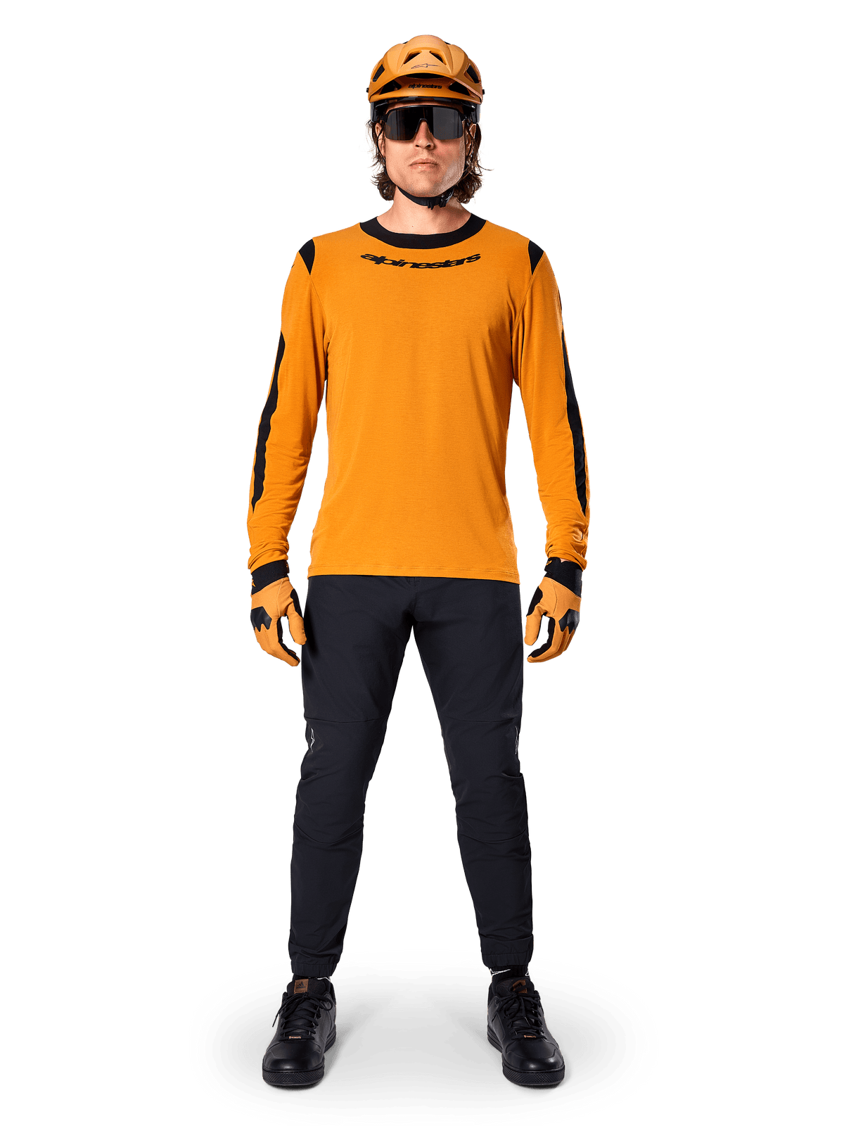 Mountain biker wearing Alpinestars A-Dura Dri Wool Long Sleeve Jersey, Dark Gold with black accents on neck and sleeves, paired with black pants, matching gold helmet, gloves, and black sunglasses, professional mountain biking gear