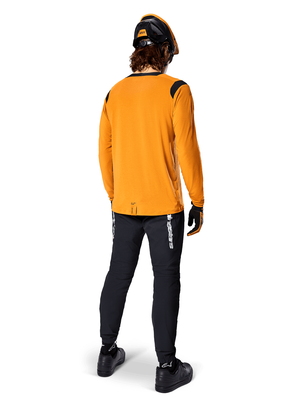 Mountain biker seen from behind wearing the Alpinestars A-Dura Dri Wool Long Sleeve Jersey in Dark Gold, black technical pants with white branding, and a coordinated black and orange helmet, performance-driven mountain bike apparel.