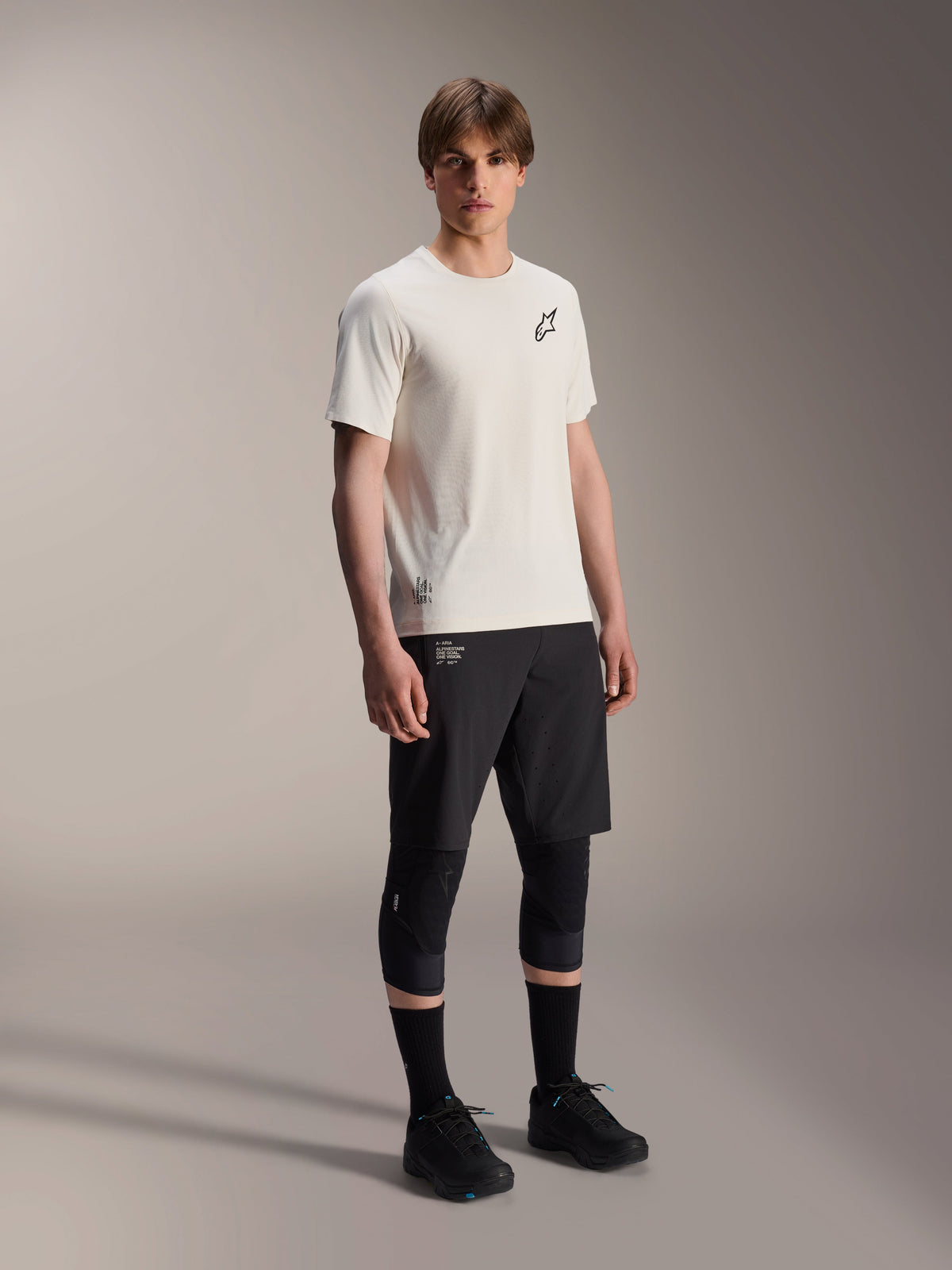 Alpinestars A-Aria Astar Jersey, Short Sleeve, Ecru, featuring black chest logo, worn with black cycling shorts and knee protectors, lightweight MTB performance gear