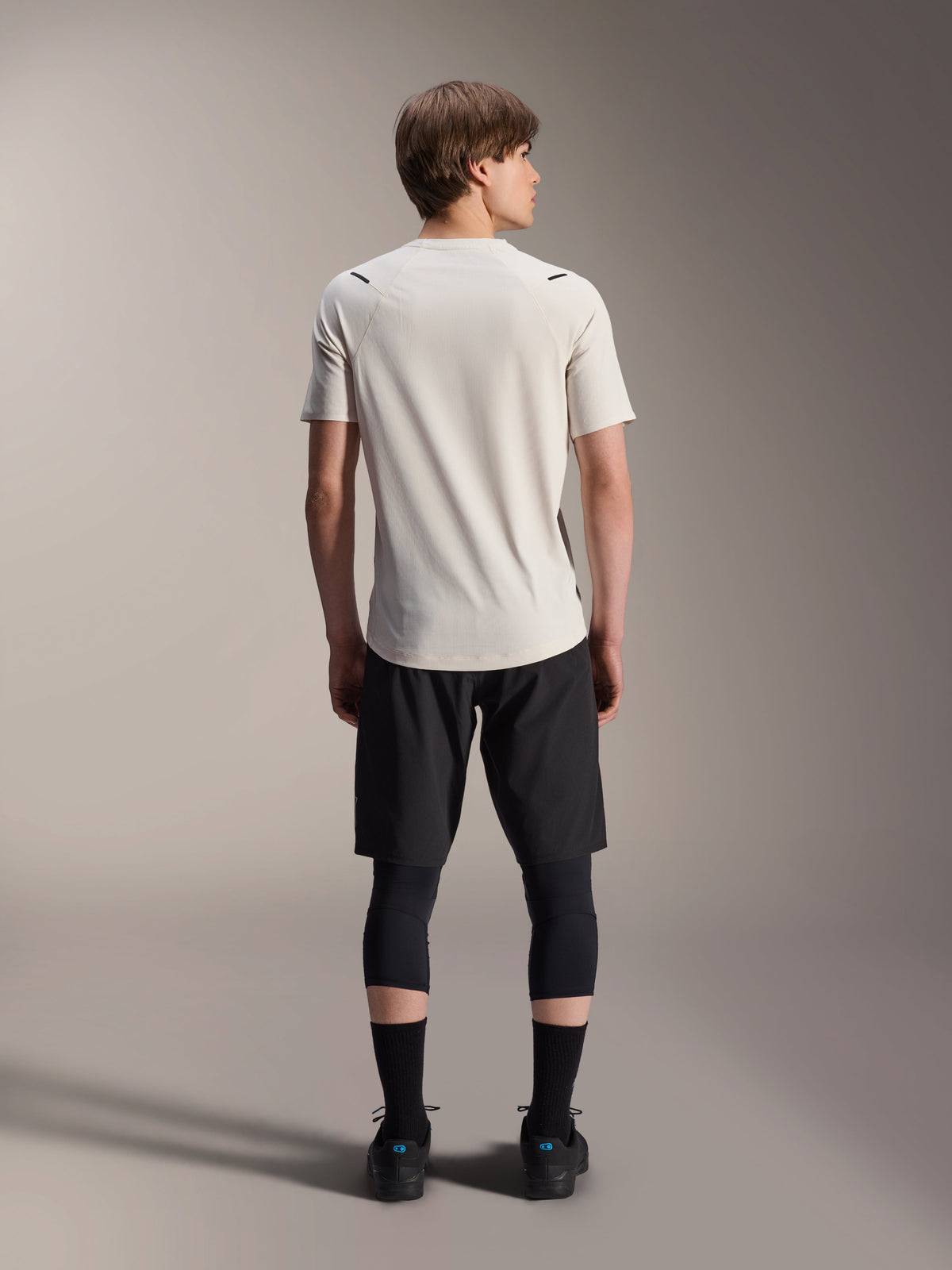 Male model from the back wearing Alpinestars A-Aria Astar Short Sleeve Jersey in Ecru, paired with black MTB shorts and protective leggings, featuring a dropped tail and performance fit for off-road trail riding.