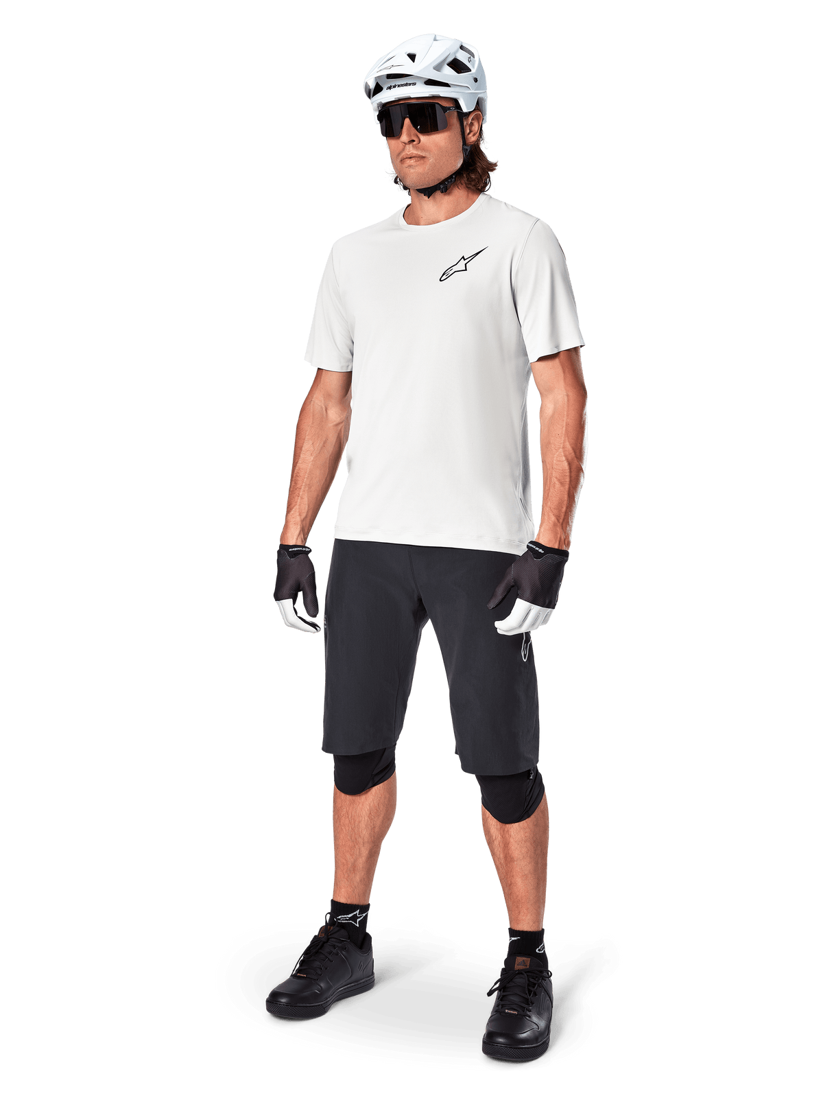MTB rider wearing Alpinestars A-Aria Astar Short Sleeve Jersey in White Dove, paired with black mountain bike shorts, white helmet, and black knee guards, featuring a small black logo on the chest, coordinated cycling gear for trail performance