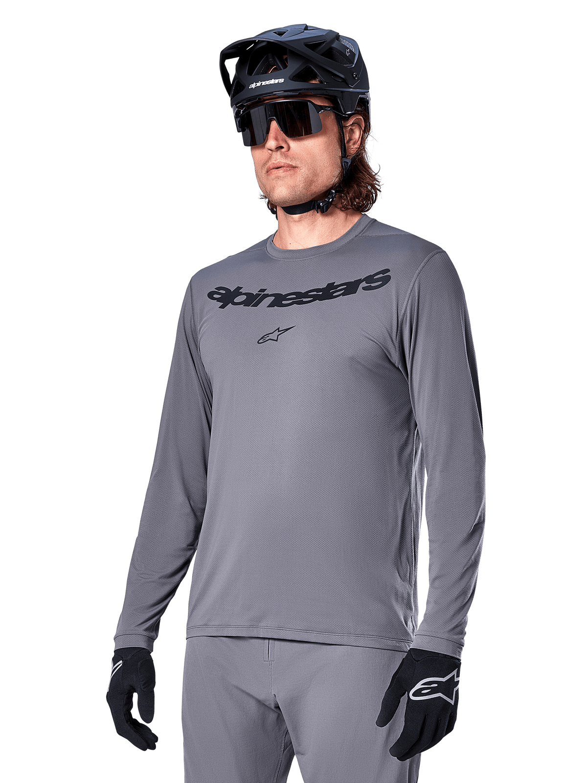 Alpinestars A-Dura Rocker Long Sleeve Jersey, Gray MTB Mountain Biking Jersey, worn with black helmet and gloves, featuring black wordmark on the chest, sporty cycling apparel for off-road riding, plain background