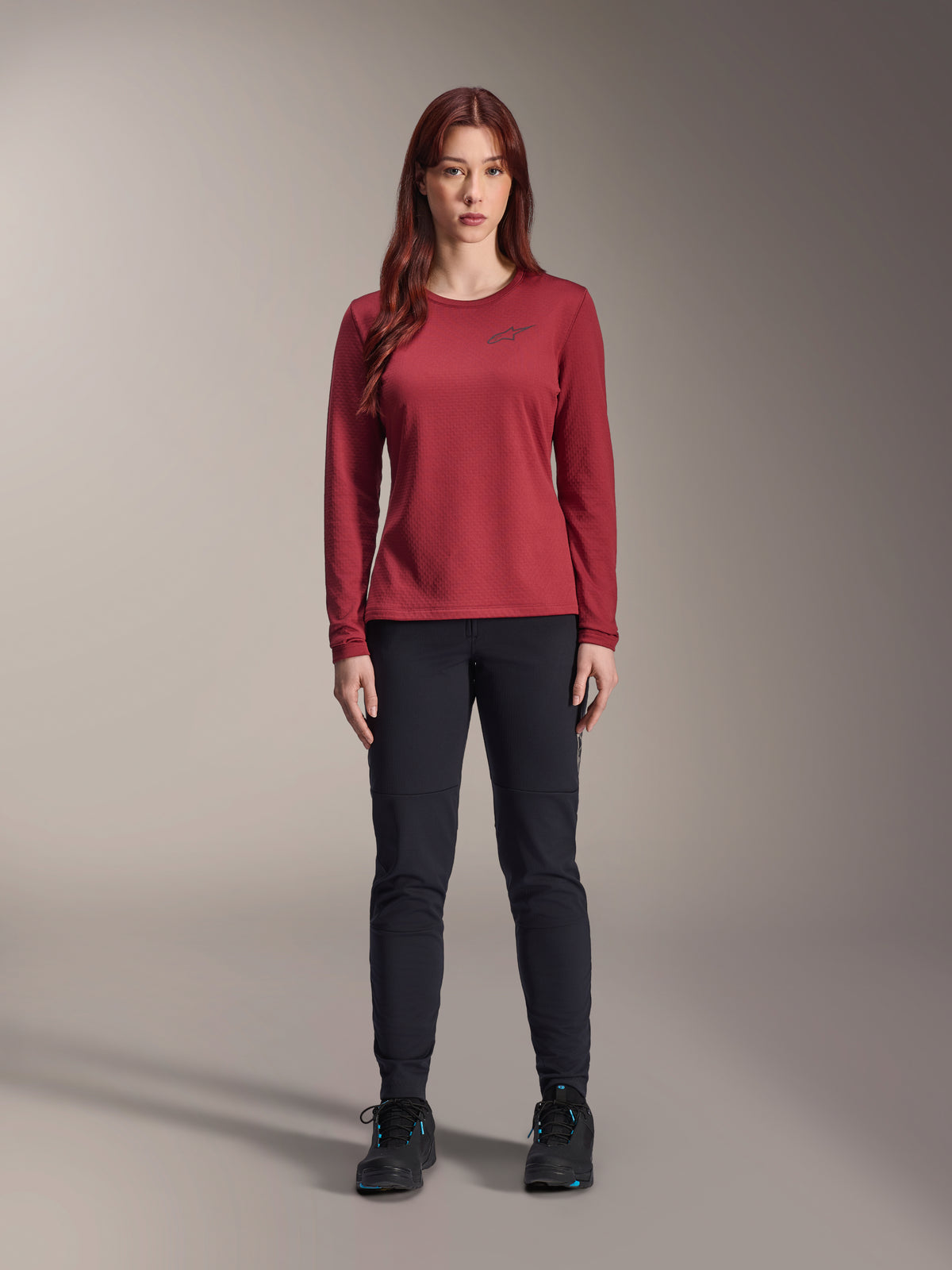 Alpinestars Woman Stella A-Dura Thermal Jersey, long-sleeve cycling jersey, Burgundy, worn by female model with black pants and black shoes, features subtle chest logo, regular fit for mountain biking