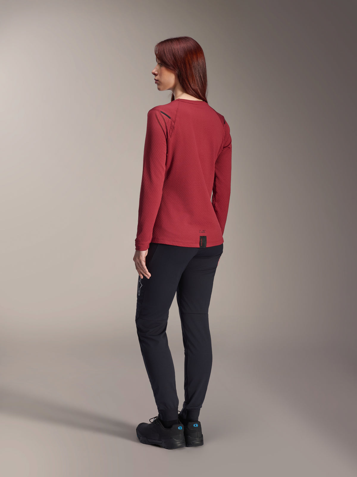 Alpinestars Stella A-Dura Thermal Jersey, Women's long-sleeve mountain bike jersey, Burgundy, back view highlighting the extended drop tail and thermal fabric texture, worn with black MTB pants and black footwear