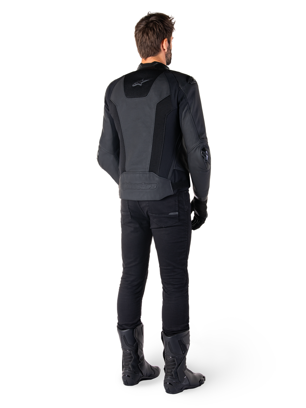 Rear view of a man wearing the Alpinestars Missile V3 Airflow Leather Jacket in Black, featuring extensive perforated panels for ventilation, paired with black riding pants and boots, showcasing a streamlined racing aesthetic.