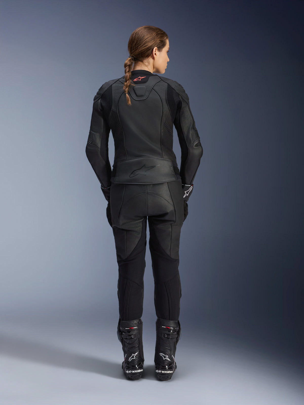 Alpinestars Women Stella GP Plus V4 Leather Jacket, Black Black, full-body rear view of a female rider wearing matching leather pants and boots, sleek minimalist design with a small red logo on the neck, tailored sport silhouette for women