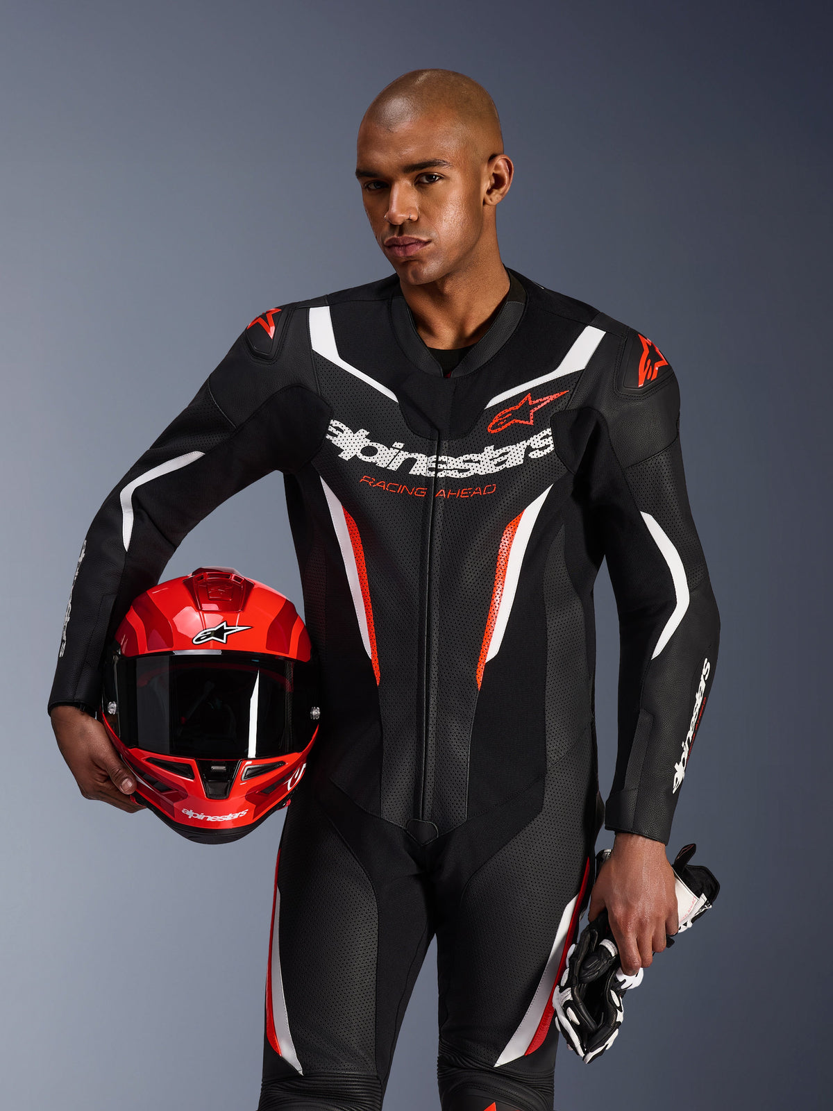 Alpinestars GP Force V2 Leather Suit, 1-Piece Motorcycle Suit, Black White and Red Fluo, worn by a model holding a red helmet and gloves, sleek racing design with perforated leather and bold branding