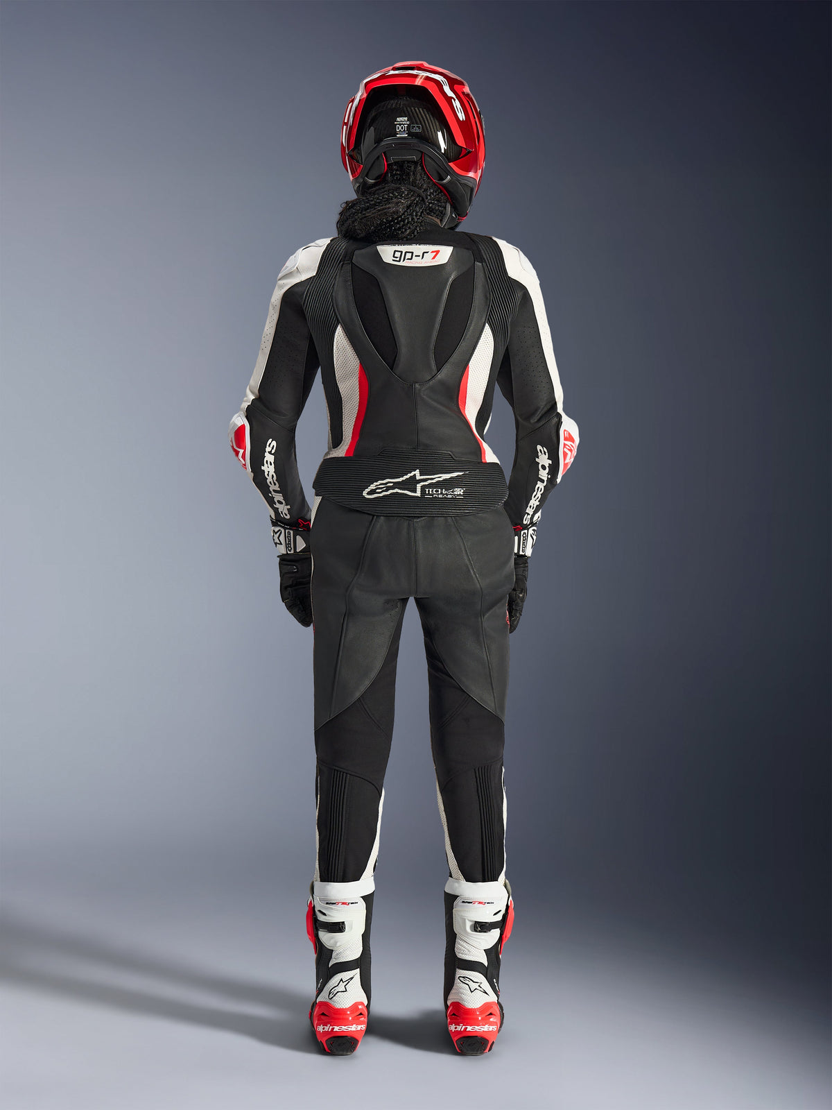 Woman Stella GP-R7 Leather Suit - 2Piece, rear view, Black White and Red Fluo, featuring aerodynamic hump with GP-R7 branding, Tech-Air Ready logo on the lower back, accordion stretch panels, and Alpinestars branding on the sleeves, worn with matching helmet and boots