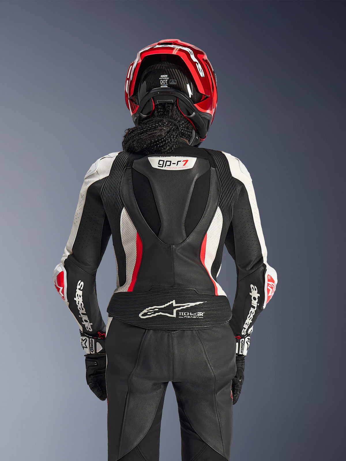 Alpinestars Woman Stella GP-R7 2-Piece Leather Suit, Black White and Red Fluo, back view of a rider wearing a red helmet and black gloves, featuring an aerodynamic hump with gp-r7 branding and Tech-Air Ready logo on the lower back.