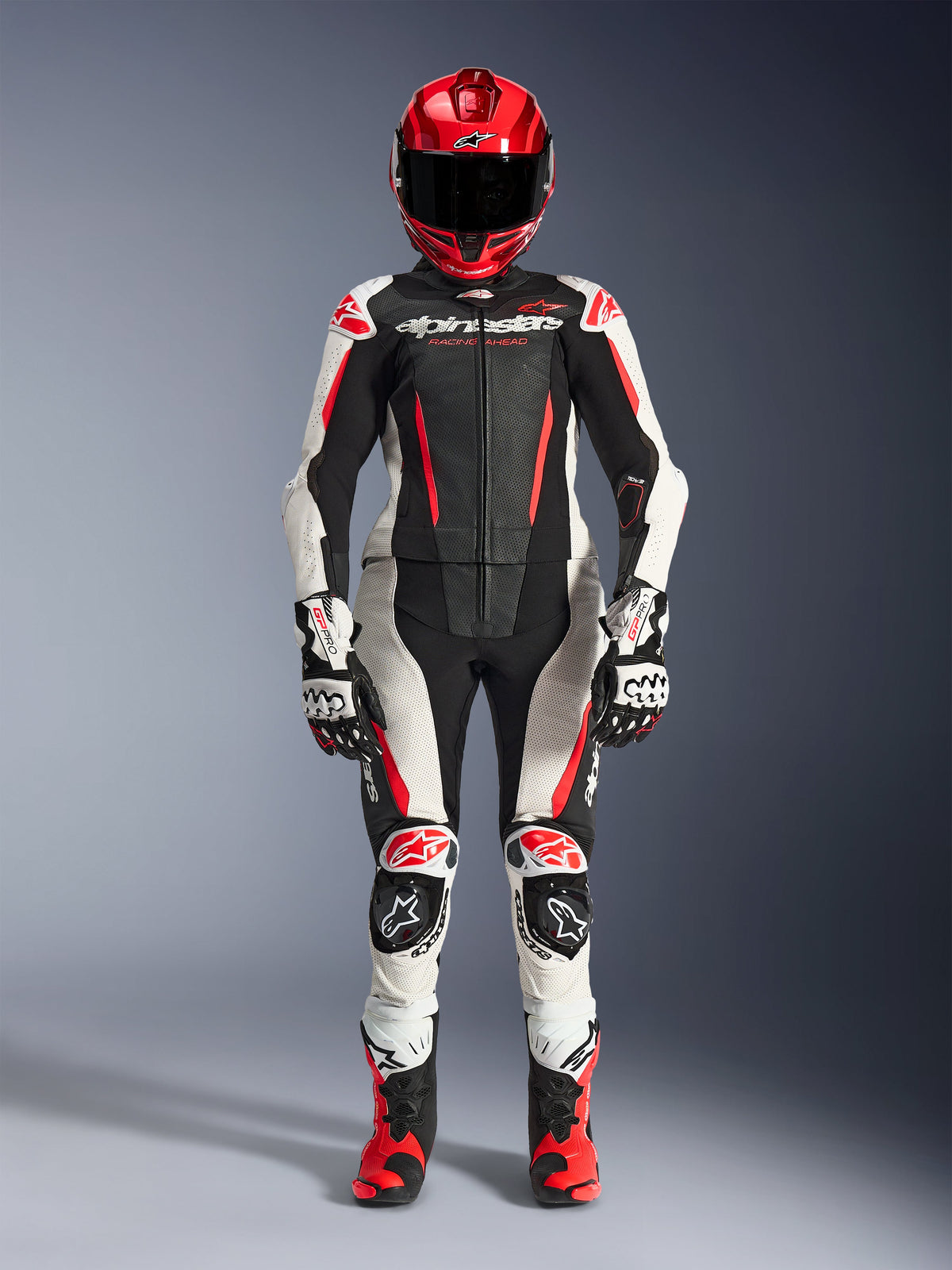 Alpinestars Woman Stella GP-R7 2-Piece Leather Suit in Black, White, and Red Fluo, full-body view of a rider wearing a matching racing helmet, gloves, and boots, featuring perforated panels and aerodynamic design for track and road riding.