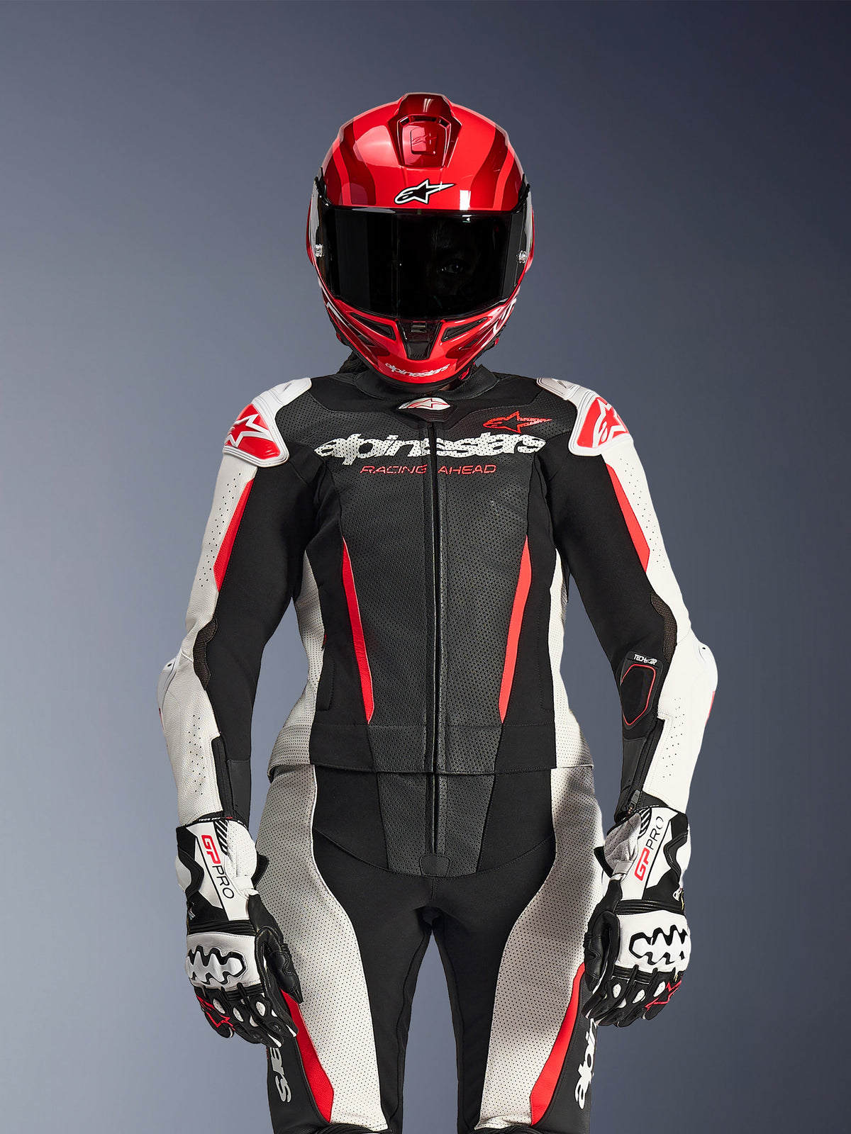 Female rider wearing Alpinestars Stella GP-R7 2-Piece Leather Suit, Black White and Red Fluo colors, featuring perforated panels and 'Racing Ahead' branding, worn with a red helmet and white/black GP Pro gloves, professional racing gear setup