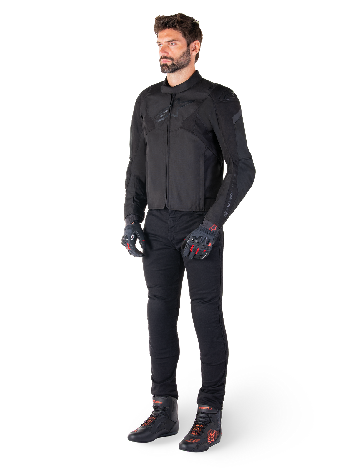 Male model wearing the Alpinestars T-Jaws V4 Waterproof Jacket in Black, paired with black riding pants, black gloves with red accents, and black motorcycle shoes, featuring a sleek sport fit and subtle branding, isolated on a white background.