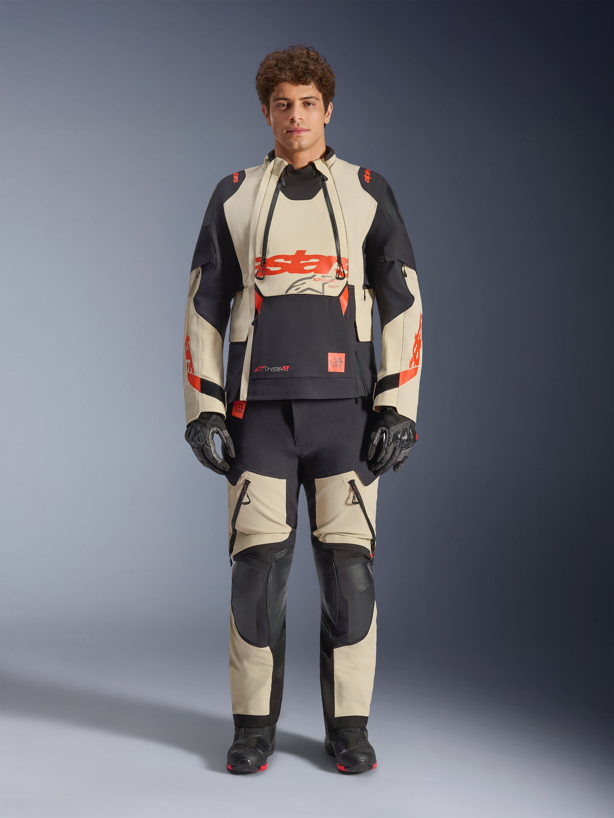 Alpinestars Halo Pro Drystar® XF Laminated Jacket, Mastic Black, adventure motorcycle jacket worn by a model with matching pants and gloves, tan and black textile panels with bold red logos, modular design for all-terrain riding