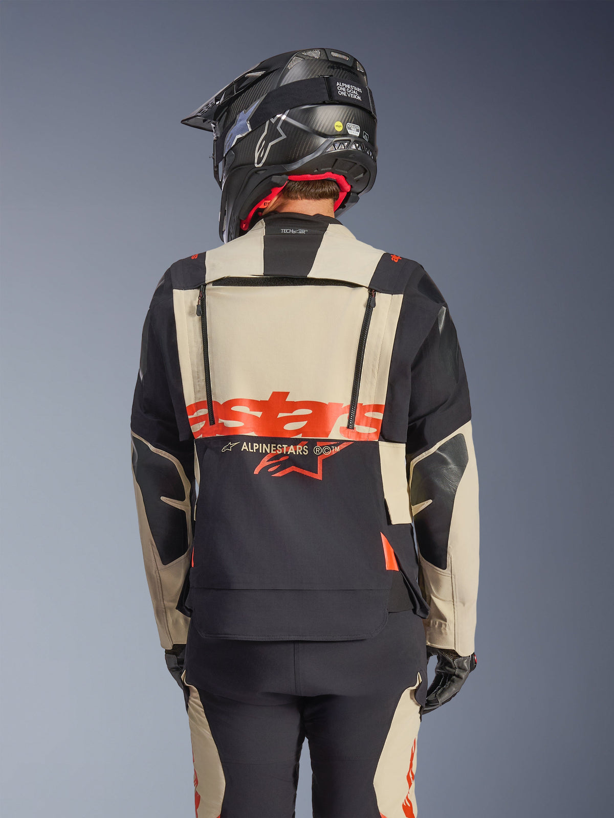 Alpinestars Halo Pro Drystar® XF Laminated Jacket in Mastic Black, rear view showing modular back panel with red logo and ventilation zippers, worn by a rider with matching adventure pants and a black helmet