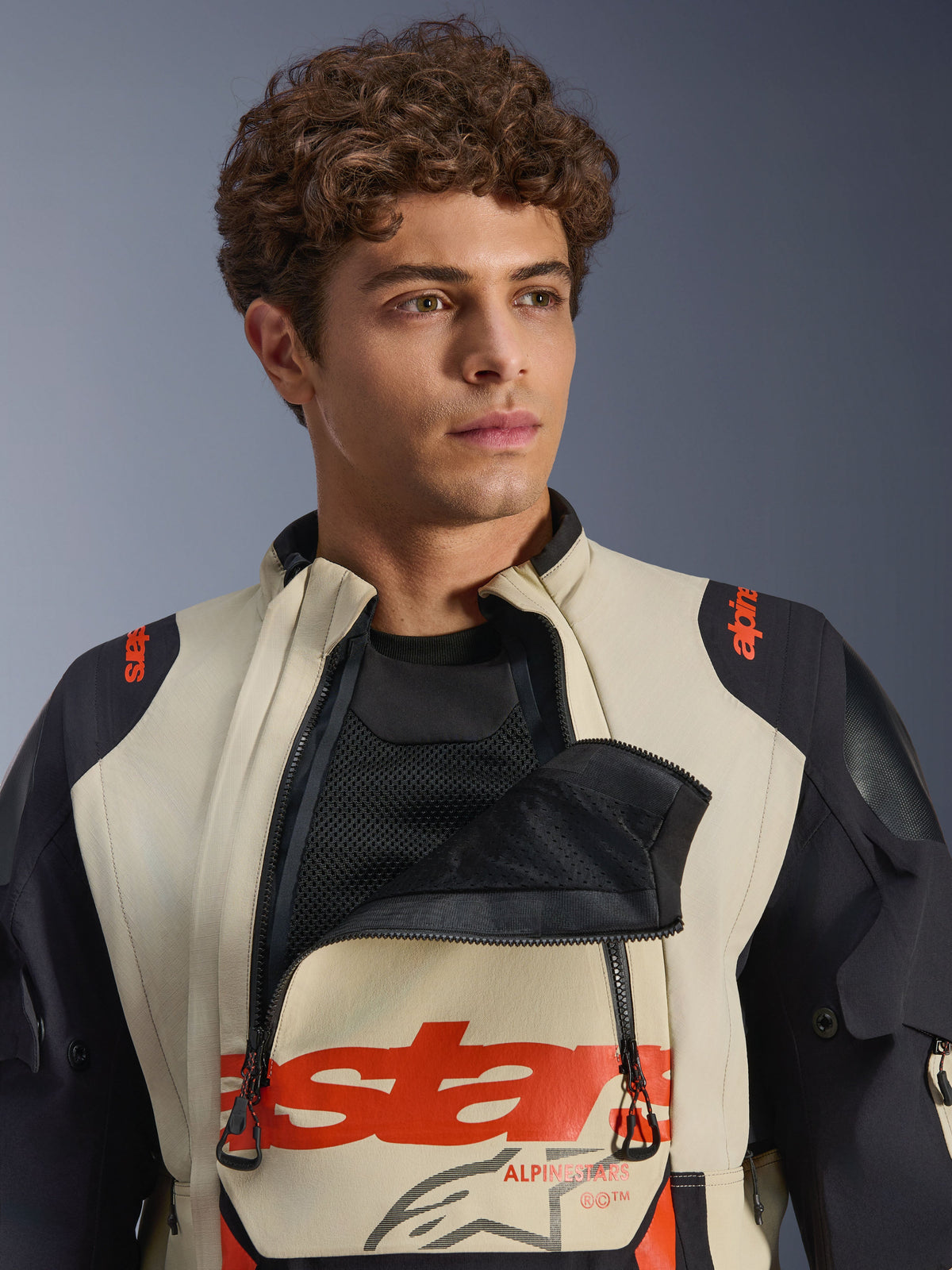 Alpinestars Halo Pro Drystar® XF Laminated Jacket in Mastic Black, male model wearing the jacket with the front chest ventilation panel unzipped to show mesh underlayer, featuring red branding and black shoulder panels, technical adventure motorcycle gear