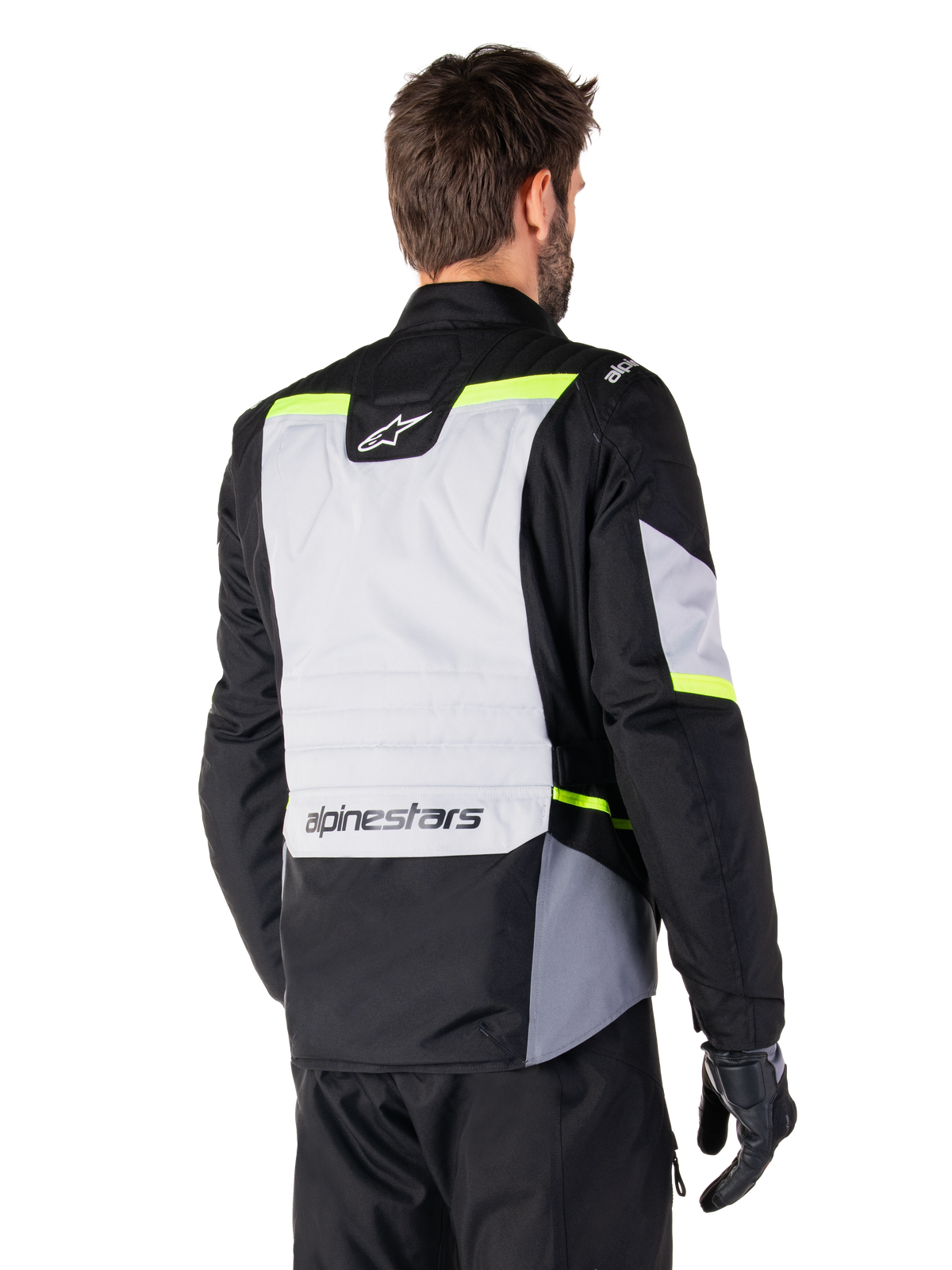 Alpinestars ST-1 Waterproof Jacket in Ice Gray Black Yellow Fluo, rear three-quarter view of a rider wearing the adventure touring jacket, featuring a large gray back panel with fluorescent yellow accents and Alpinestars branding, paired with black riding pants and gloves