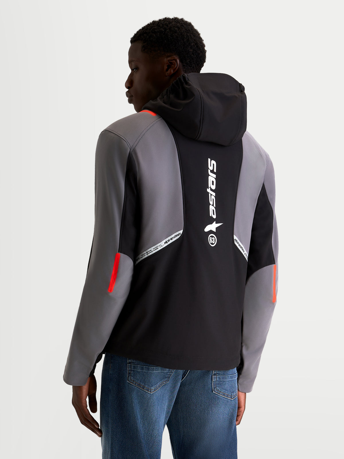 Alpinestars C-5 Drystar® Jacket, men's urban motorcycle softshell jacket in black and dark gray, rear view on a model showing the integrated hood, large reflective Alpinestars branding on the back, and waterproof textile construction.