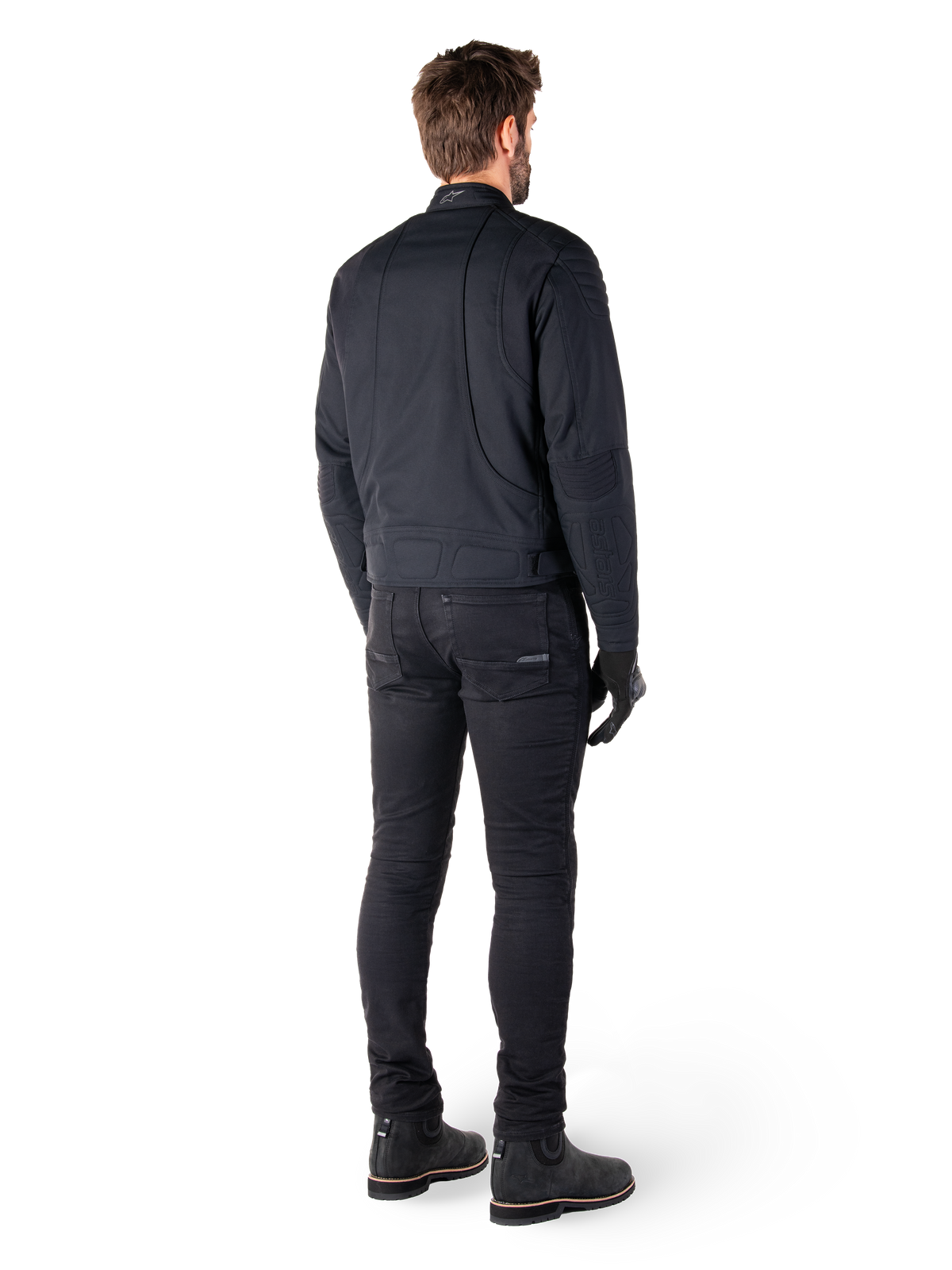 Rear view of a rider wearing the Alpinestars Clayton WR Jacket in Black, featuring quilted elbow and shoulder panels, ergonomic curved stitching, and reflective collar detailing, paired with black riding pants and boots for an urban motorcycle look.