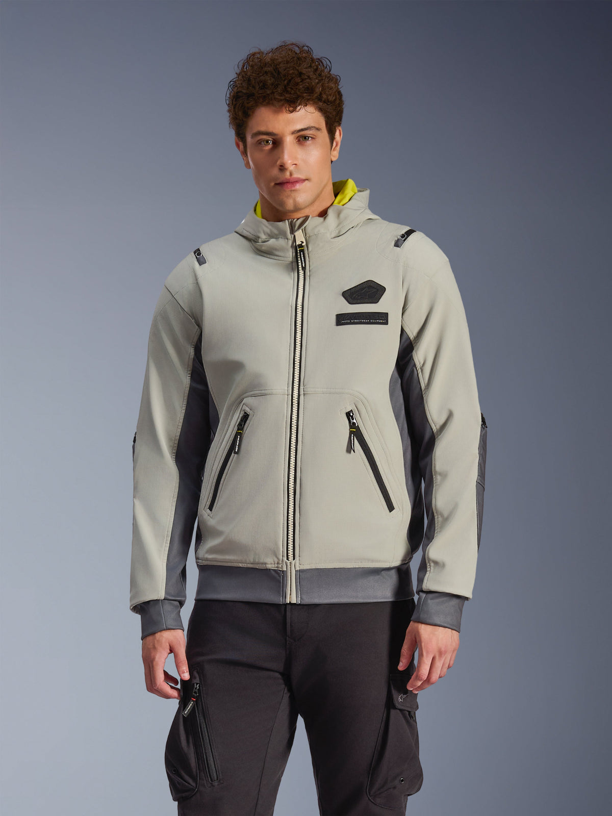 Alpinestars Moblast Waterproof Jacket, light gray and dark gray urban motorcycle hoodie with yellow hood lining, front pockets and black zippers, worn with black cargo pants, modern sporty design