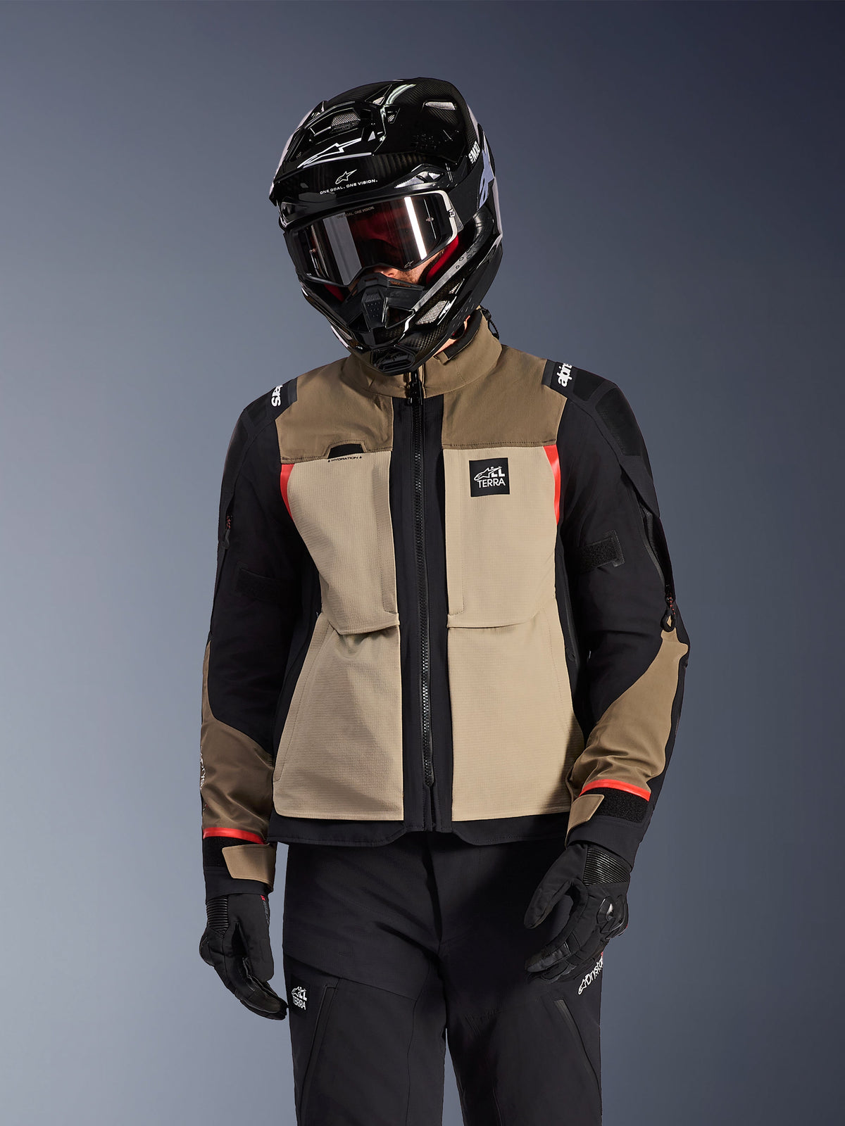 Alpinestars Andes Pro Drystar® XF Jacket, Adventure Touring Motorcycle Jacket, Walnut Aluminum beige and brown with black panels and red accents, worn with a black Alpinestars helmet and goggles, technical outdoor motorcycle gear