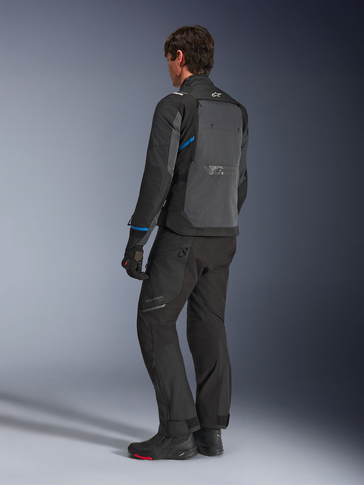 Alpinestars Cusco Drystar® Jacket, Black and Deep Gray, back three-quarter view showing large rear ventilation panel and blue accents on sleeves, worn with black motorcycle pants and boots for a complete touring outfit.