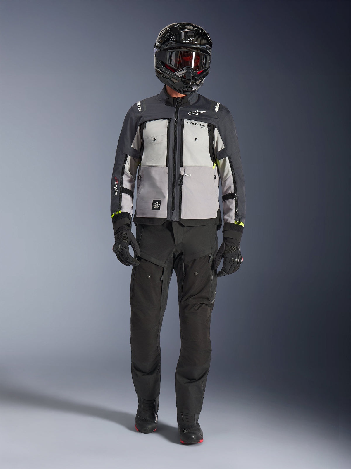 Alpinestars Cusco Drystar® Jacket, Ice Gray Mid Gray Deep Gray, adventure motorcycle jacket worn with black riding pants, black gloves, and a black helmet with goggles, featuring color-blocked gray panels and technical detailing for road and adventure touring.