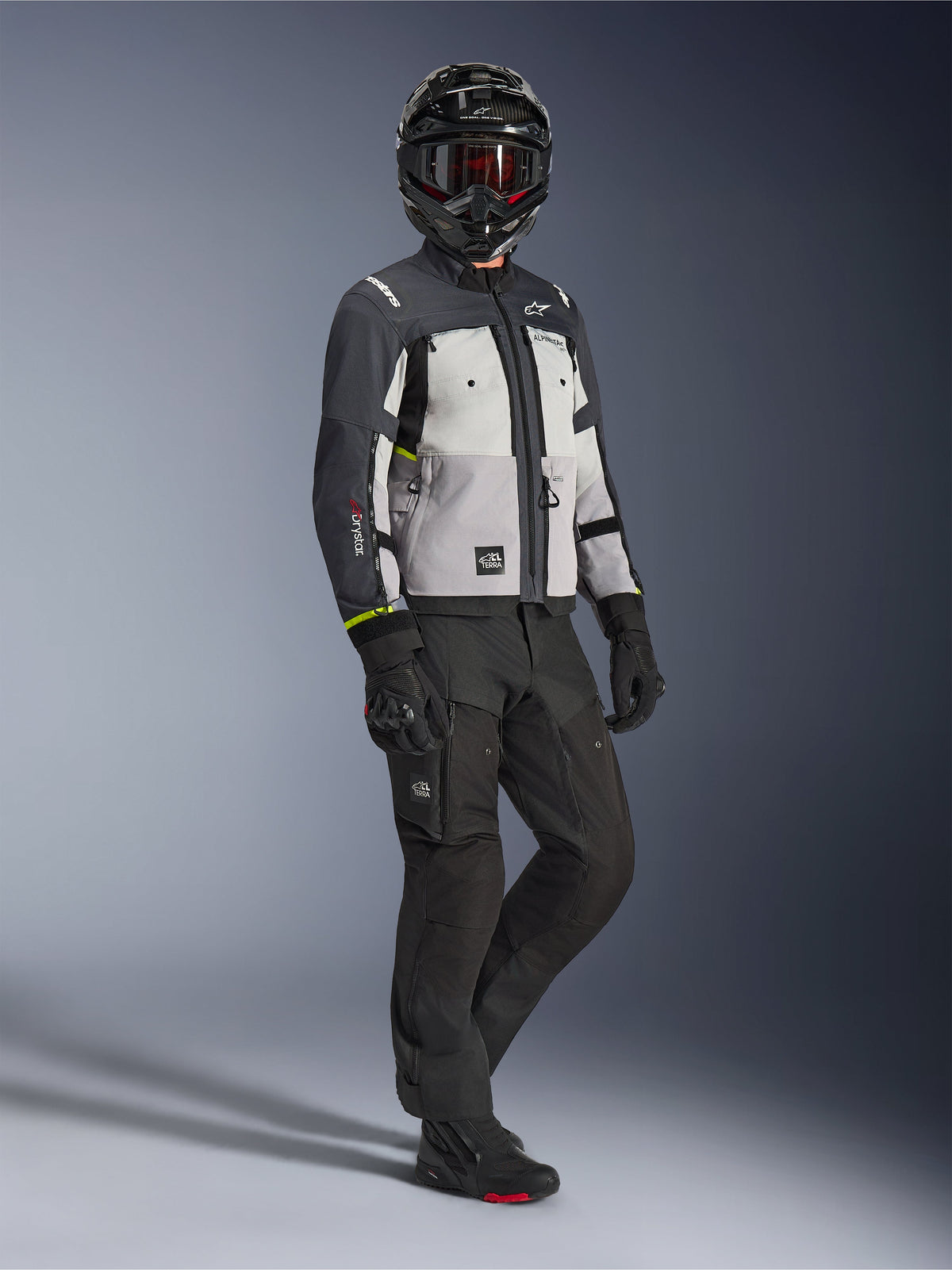Alpinestars Cusco Drystar® Jacket in Ice Gray Mid Gray Deep Gray, full-body shot of a rider wearing complete adventure gear including a black helmet with red goggles, matching black pants, and gloves, textile motorcycle jacket with direct ventilation panels and waterproof membrane