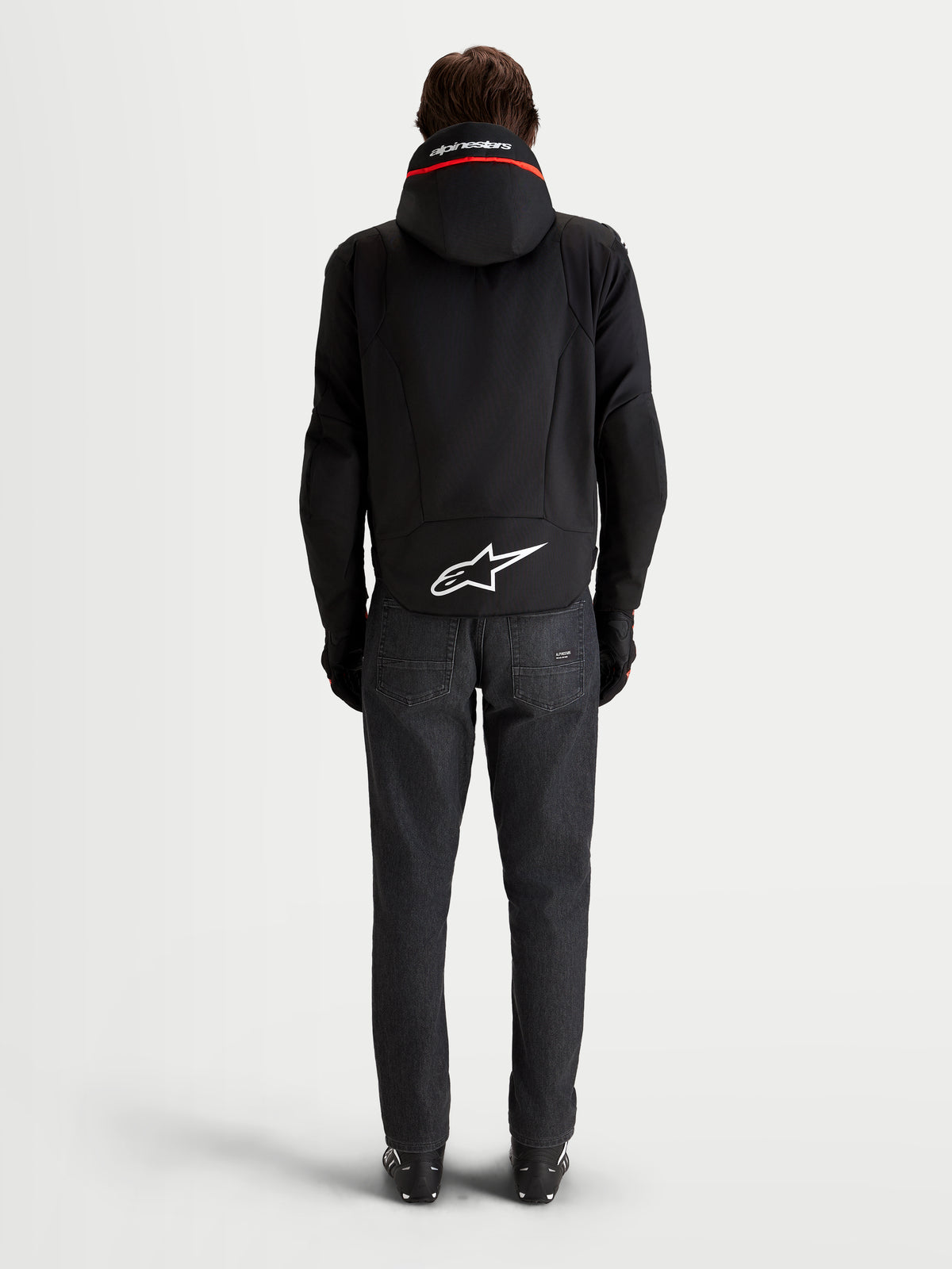 Alpinestars Zaca V2 Waterproof Jacket, Men's Black waterproof motorcycle jacket viewed from the rear, showing the integrated hood, extended rear hem with a white Astar logo, and dark denim jeans