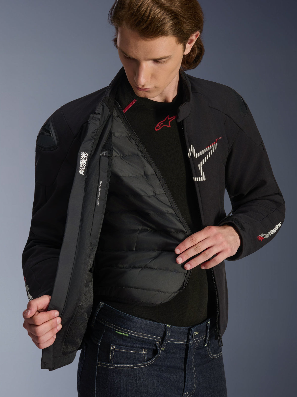 Alpinestars SMX Waterproof Jacket in Black White and Bright Red, worn by a man and unzipped to reveal the quilted detachable thermal liner, featuring external DFS lite shoulders and white logo details, performance motorcycle road gear