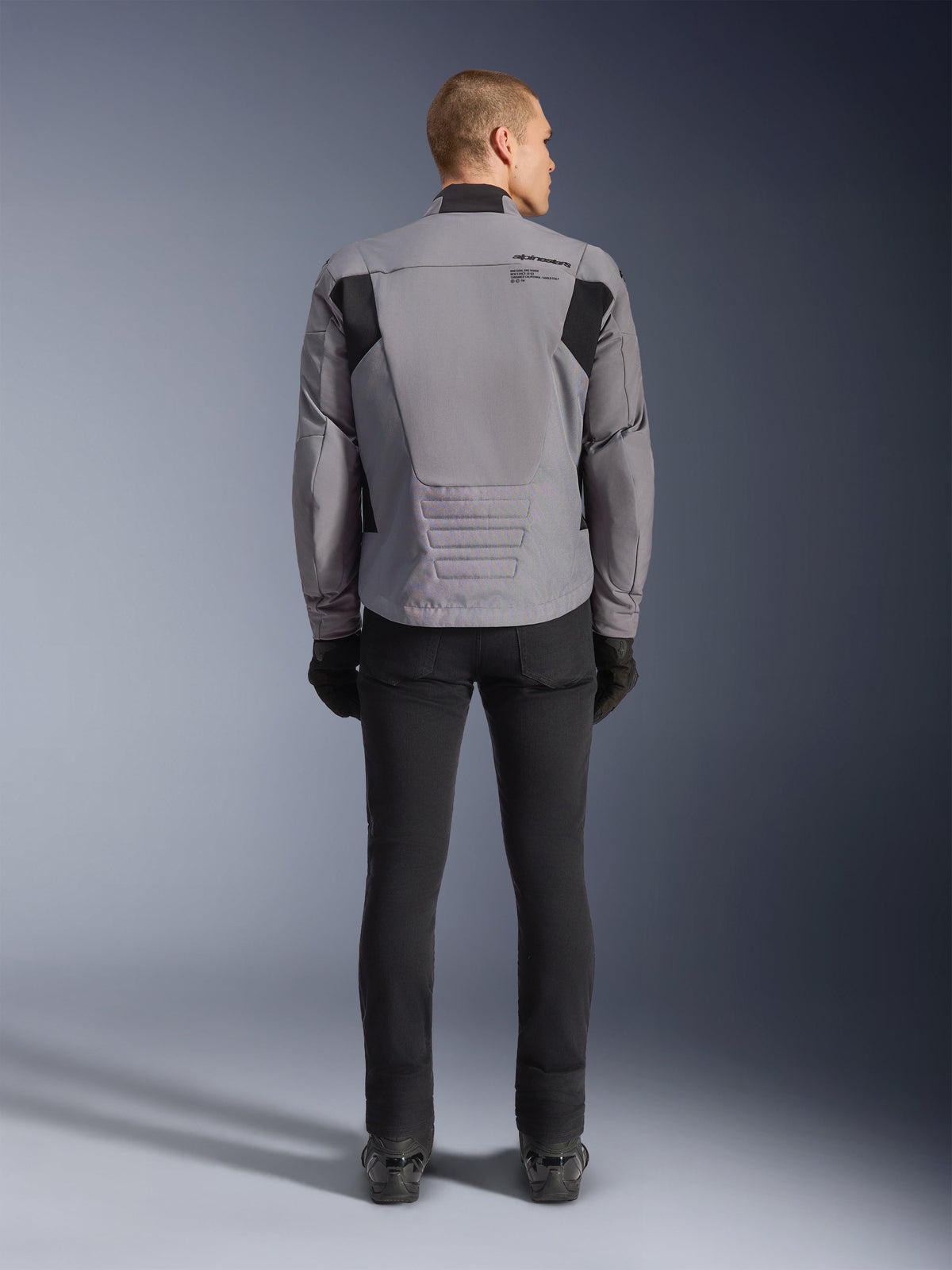 Alpinestars SMX Waterproof Jacket, Rear view, Dark Gray and Black, featuring black textile panels on shoulders and a sport-fit design, paired with black pants and gloves for a complete motorcycling look