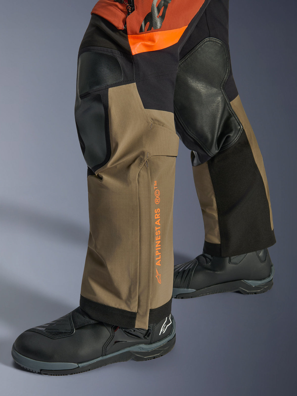 Alpinestars Halo Pro Drystar® XF Laminated Pants, Adventure Motorcycle Pants, Walnut Rust and Black, detail shot featuring reinforced knee panels and orange branding, worn with black touring boots, durable textile construction for all-terrain riding